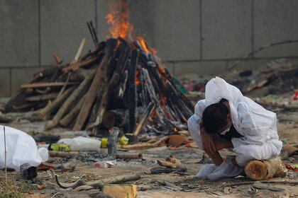 Un hombre llora mientras se sienta junto a la pira ardiente de un familiar, que murió de la enfermedad del coronavirus (COVID-19), durante su cremación, en un crematorio en Nueva Delhi, India, el 5 de mayo de 2021. REUTERS/Adnan Abidi