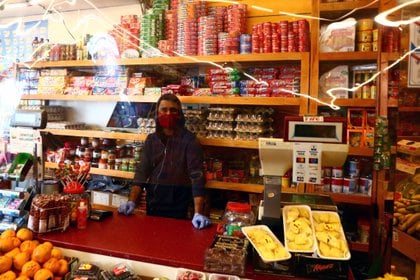 Empleado con mascarilla espera clientes detrás de una cortina de plástico en una tienda de alimentación en Madrid (REUTERS / Sergio Pérez)