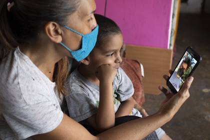 En esta imagen del 27 de abril de 2020, Daniel se sienta en el regazo de su madre en su departamento de Caracas, Venezuela, durante una videollamada con su padre, Misael Cocho. Cocho emigró a Perú y empezó a enviar dinero a su madre y a su hijo con trabajos esporádicos, pero en cuanto consiguió un empleo más estable, los casos del nuevo coronavirus se dispararon. Perdió su empleo. (AP Foto/Ariana Cubillos)