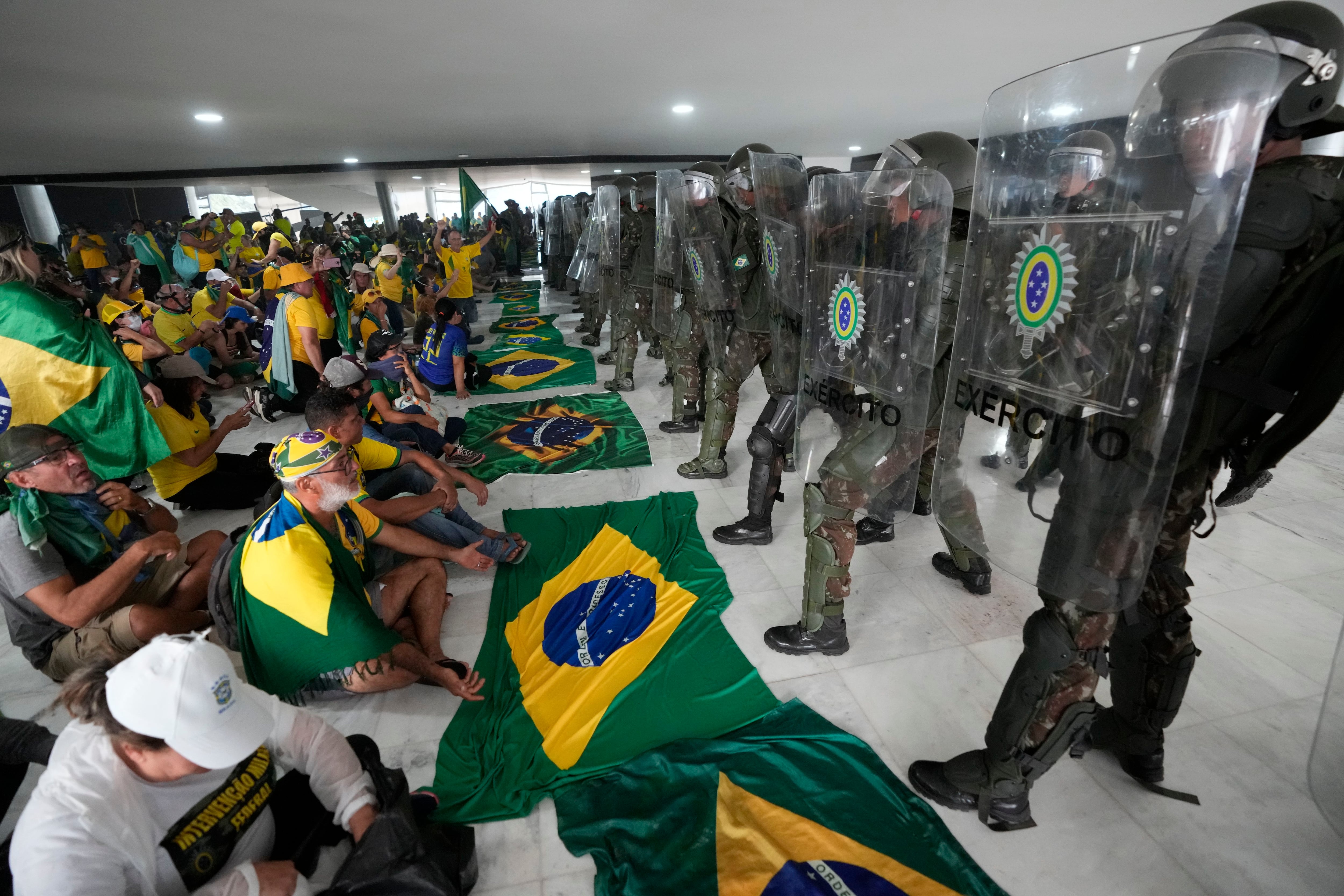 Simpatizantes de Bolsonaro sentados frente a una hilera de policías militares dentro del Palacio de Planalto, luego de que se metieron al sitio oficial de trabajo del presidente, el domingo 8 de enero de 2023, en Brasilia (AP Foto/Eraldo Peres/Archivo)