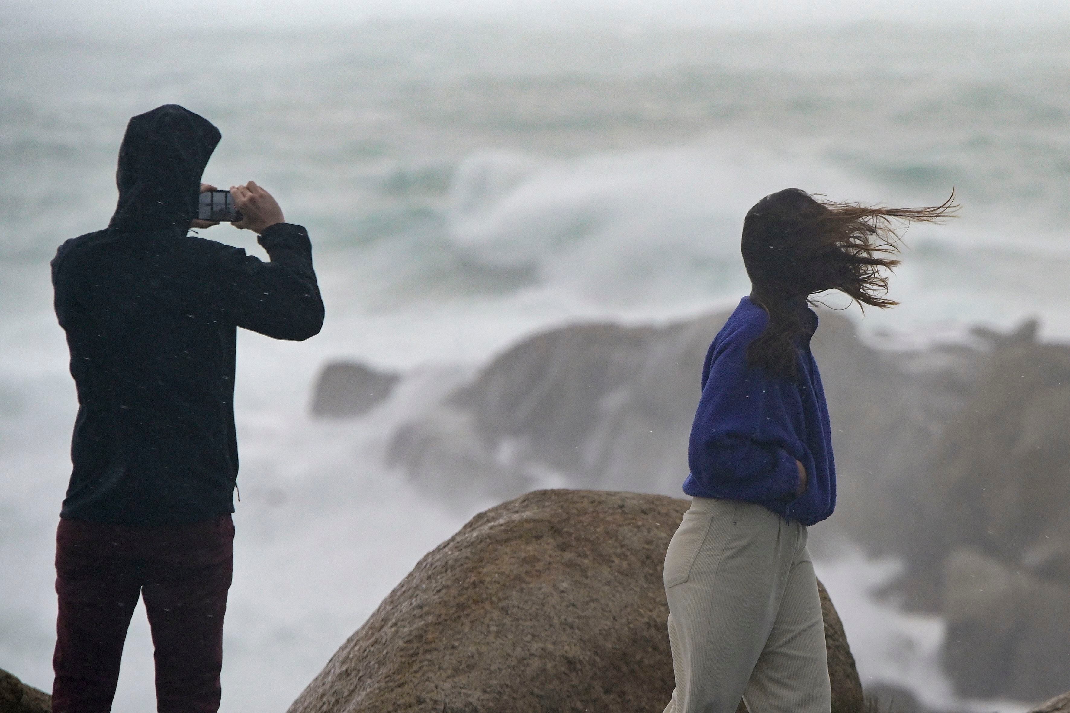 Una persona fotografía el mar embravecido, mientras el viento mueve la melena a su acompañante. (M. Dylan / Europa Press)