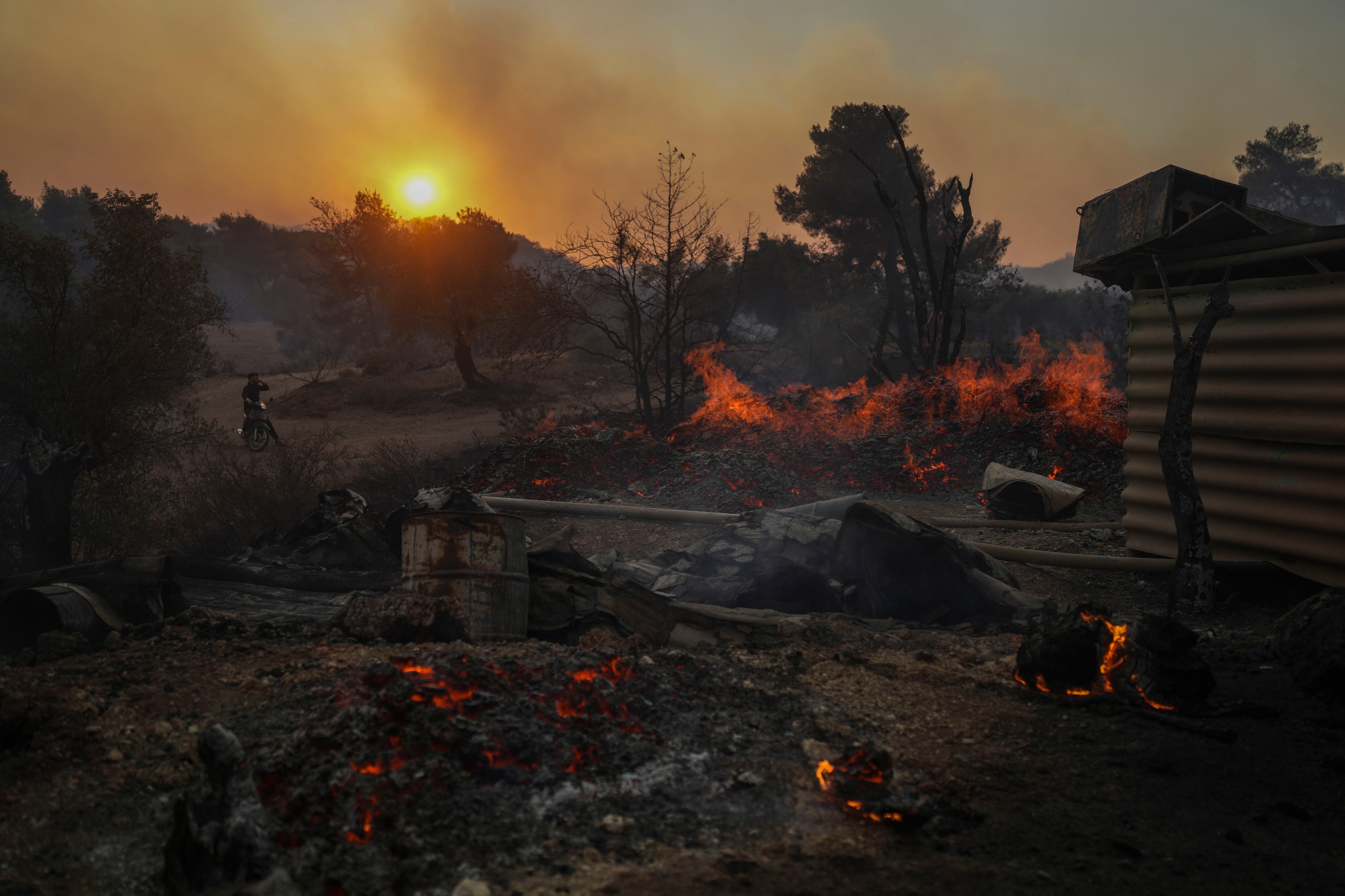 Un hombre en una motocicleta observa un astillero en llamas en Mandra, al oeste de Atenas, el martes 18 de julio de 2023 (AP/Petros Giannakouris)