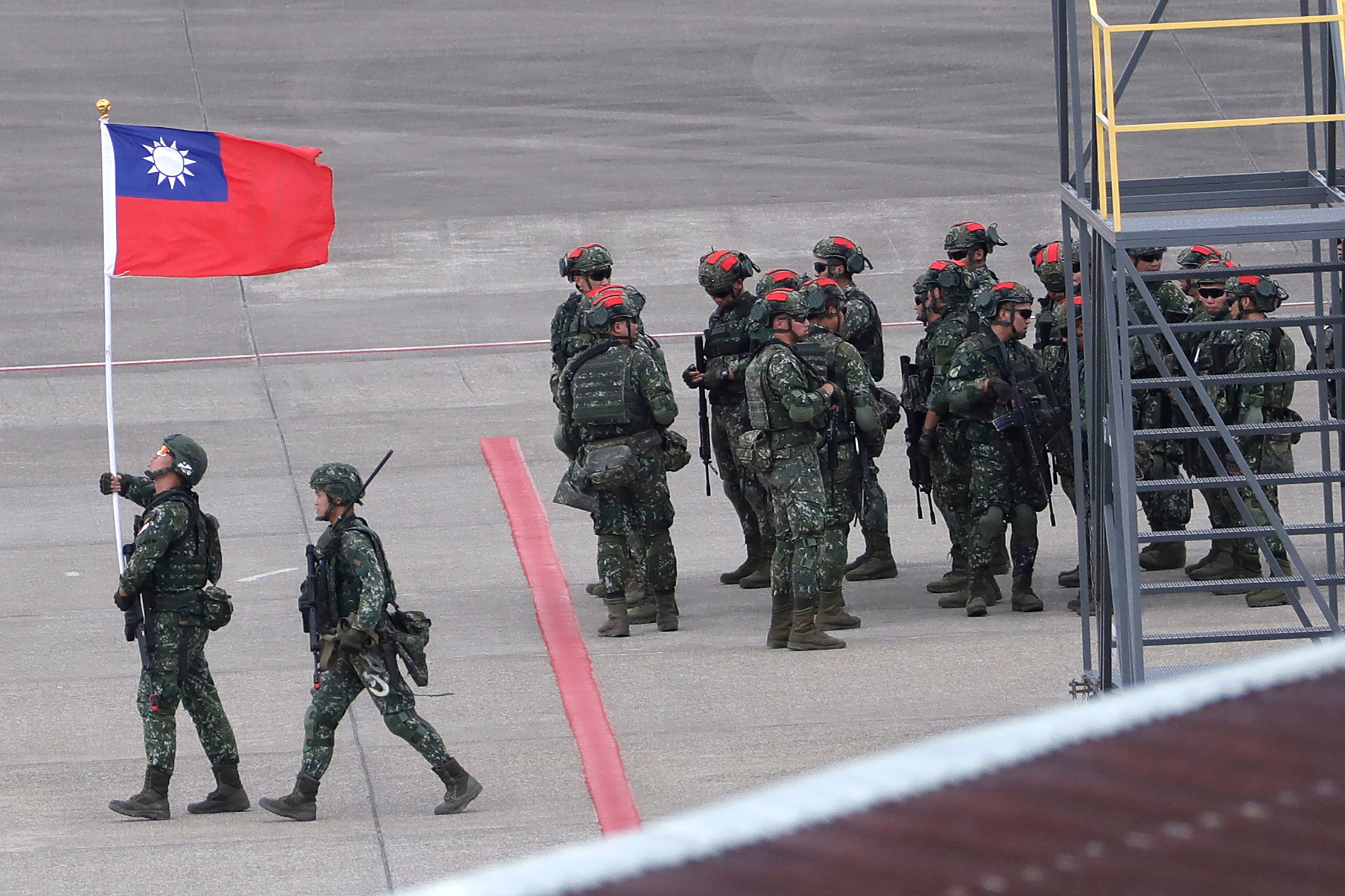 Un soldado taiwanés sostiene una bandera de Taiwán cerca de un grupo de soldados con marcas rojas en sus cascos porque se harán pasar por enemigos durante las maniobras anuales Han Kuang, que simulan un ataque a un aeródromo, en el aeropuerto internacional Taoyuan, en Taoyuan, Taiwán. (AP Foto/Chiang Ying-ying, archivo)