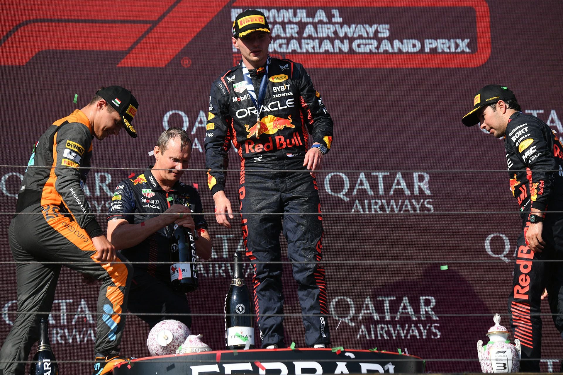Lando Norris, Max Verstappen y Sergio Pérez miran cómo quedó el trofeo roto (Photo by Ferenc ISZA / AFP)