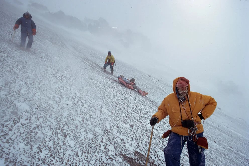 Hombre escalando montaña con mochila en la espalda y cuerdas en la mano
