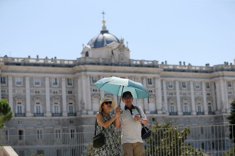 Turistas se resguardan del sol bajo una sombrilla cerca del Palacio Real de Madrid (Reuters)