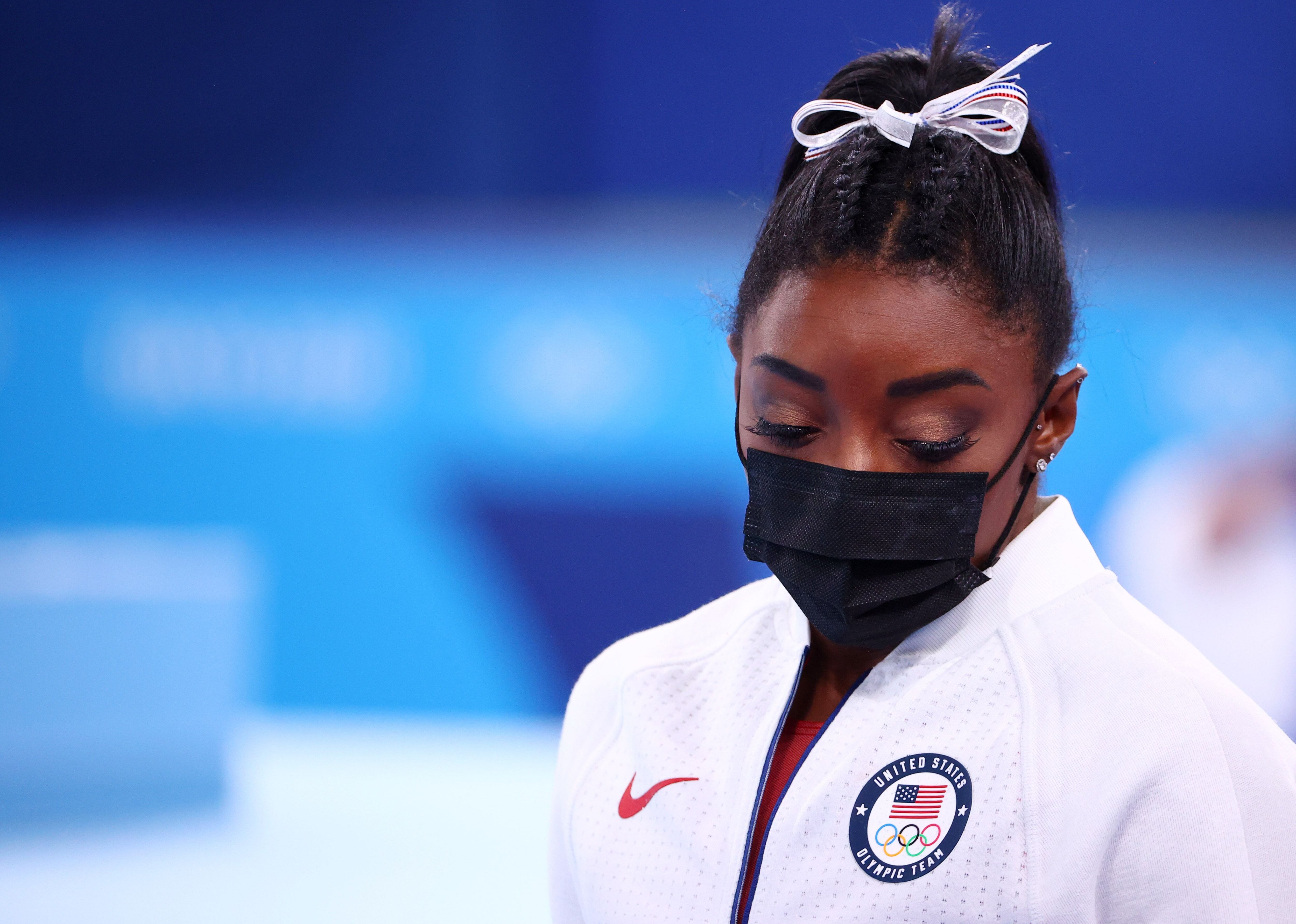 Simone Biles de los Estados Unidos con una máscara protectora mira hacia abajo. 