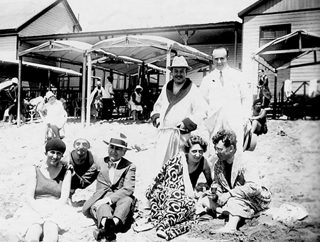 Una postal de turistas en la playa en 1930, durante la segunda etapa de crecimiento de Mar del Plata: desde el gobierno de la provincia de Buenos Aires se llevó a cabo un plan de obras públicas: la pavimentación de la ruta 2, y una década más tarde la inauguración del balneario de Playa Grande