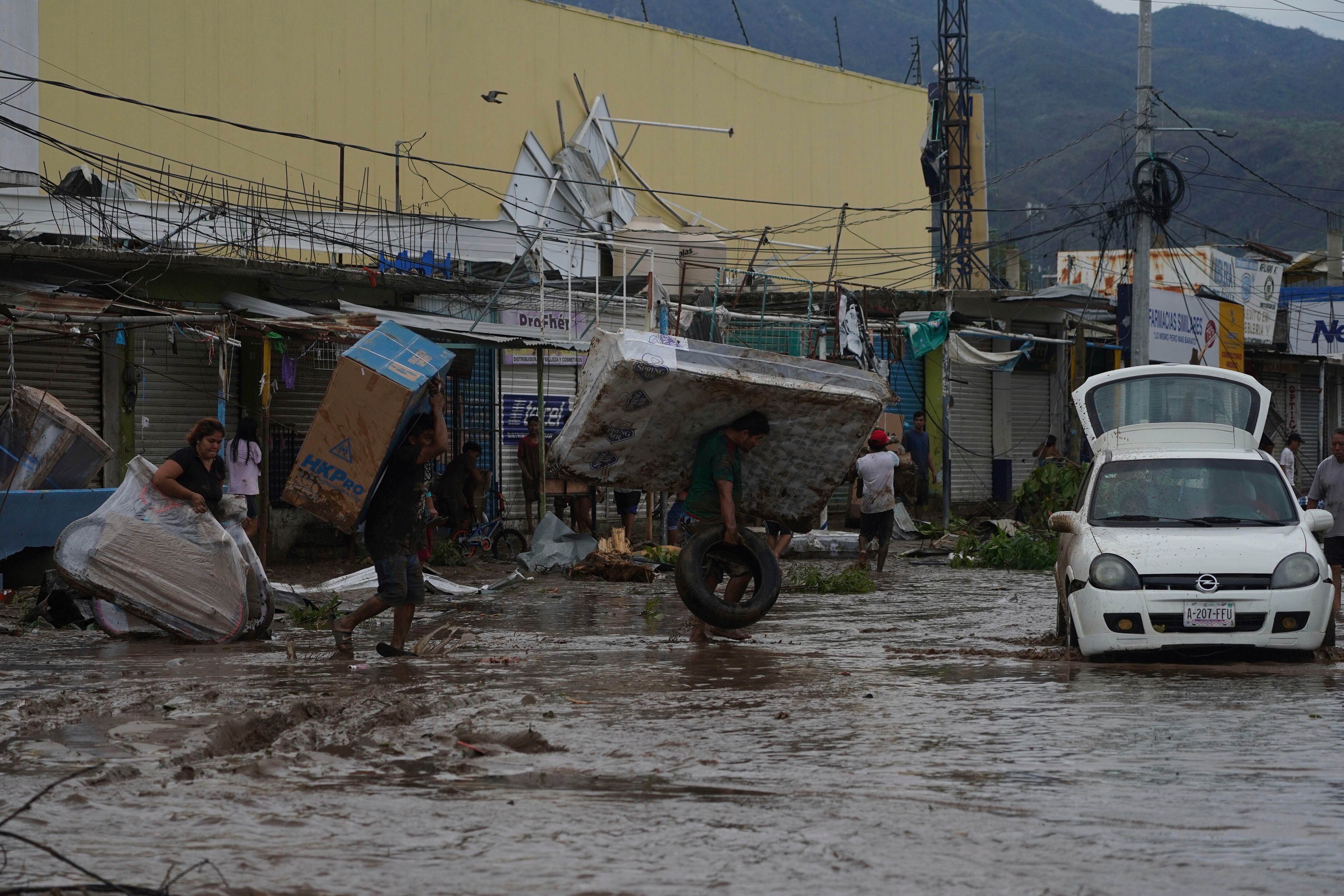 Varias personas caminan con objetos saqueados en una tienda en un centro comercial luego del paso del huracán Otis por Acapulco, México, el 25 de octubre de 2023. (AP Foto/Marco Ugarte)