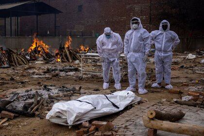 Hombres con trajes de protección permanecen junto al cuerpo de su familiar, fallecido por la enfermedad del coronavirus (COVID-19), antes de su cremación en un terreno del crematorio en Nueva Delhi, India, el 4 de mayo de 2021. REUTERS/Danish Siddiqui