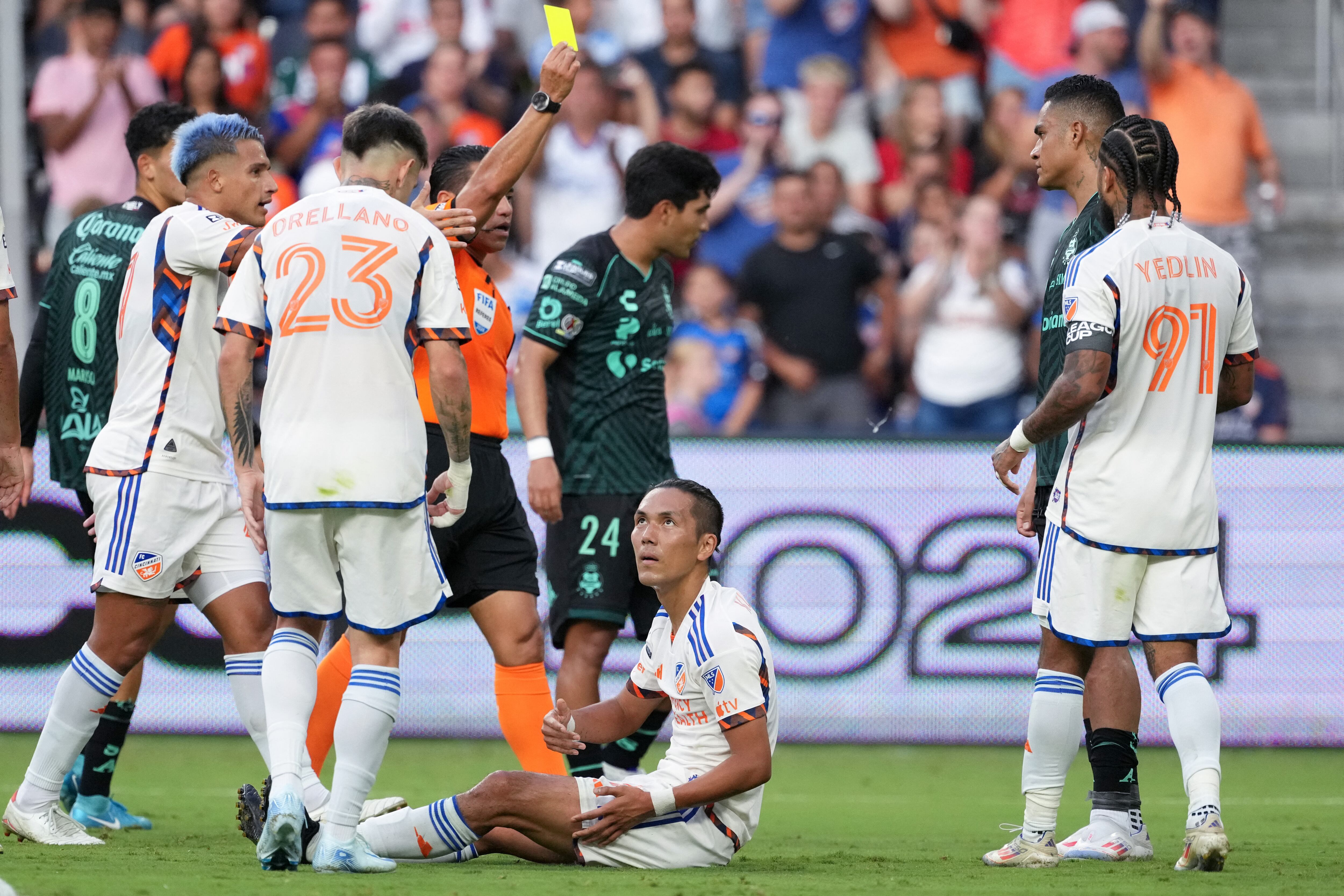 Aug 9, 2024; Cincinnati, Ohio, USA; Santos Laguna defender Santiago Nunez (4) (right) is issued a yellow card after fouling FC Cincinnati forward Yuya Kubo (7) (center) during the second half of a Leagues Cup match between FC Cincinnati and Santos Laguna at TQL Stadium. Mandatory Credit: Kareem Elgazzar-USA TODAY Sports