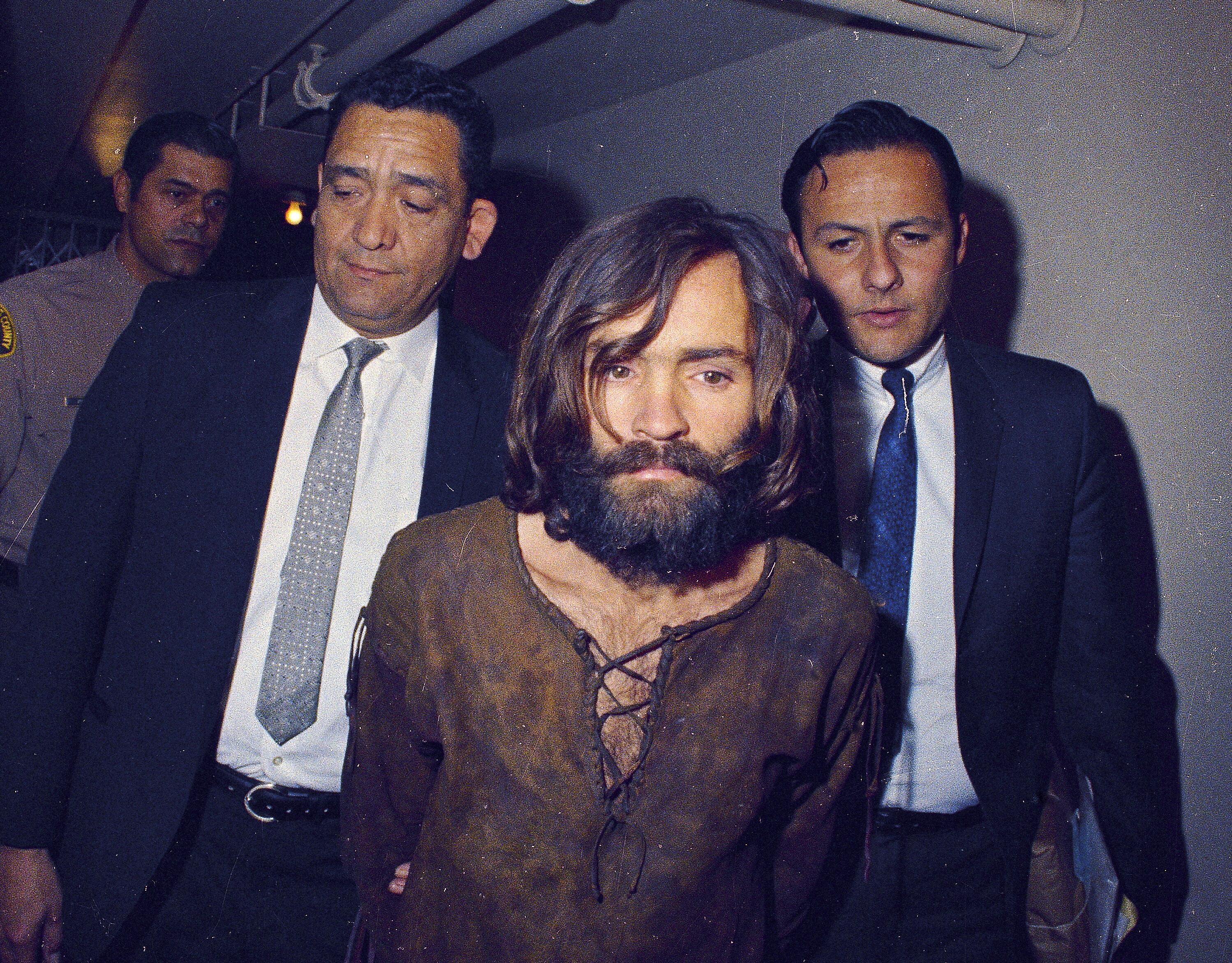 Charles Manson es escoltado a un tribunal para escuchar la lectura de cargos por cargos de asociación ilícita y asesinato en relación con el homicidio de Sharon Tate en Los Ángeles en 1969 (AP Foto/Archivo)