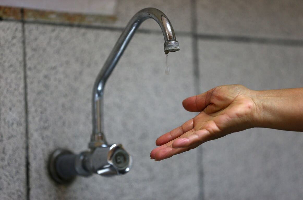 Una persona tratando de obtener agua, pero el servicio se cortó.