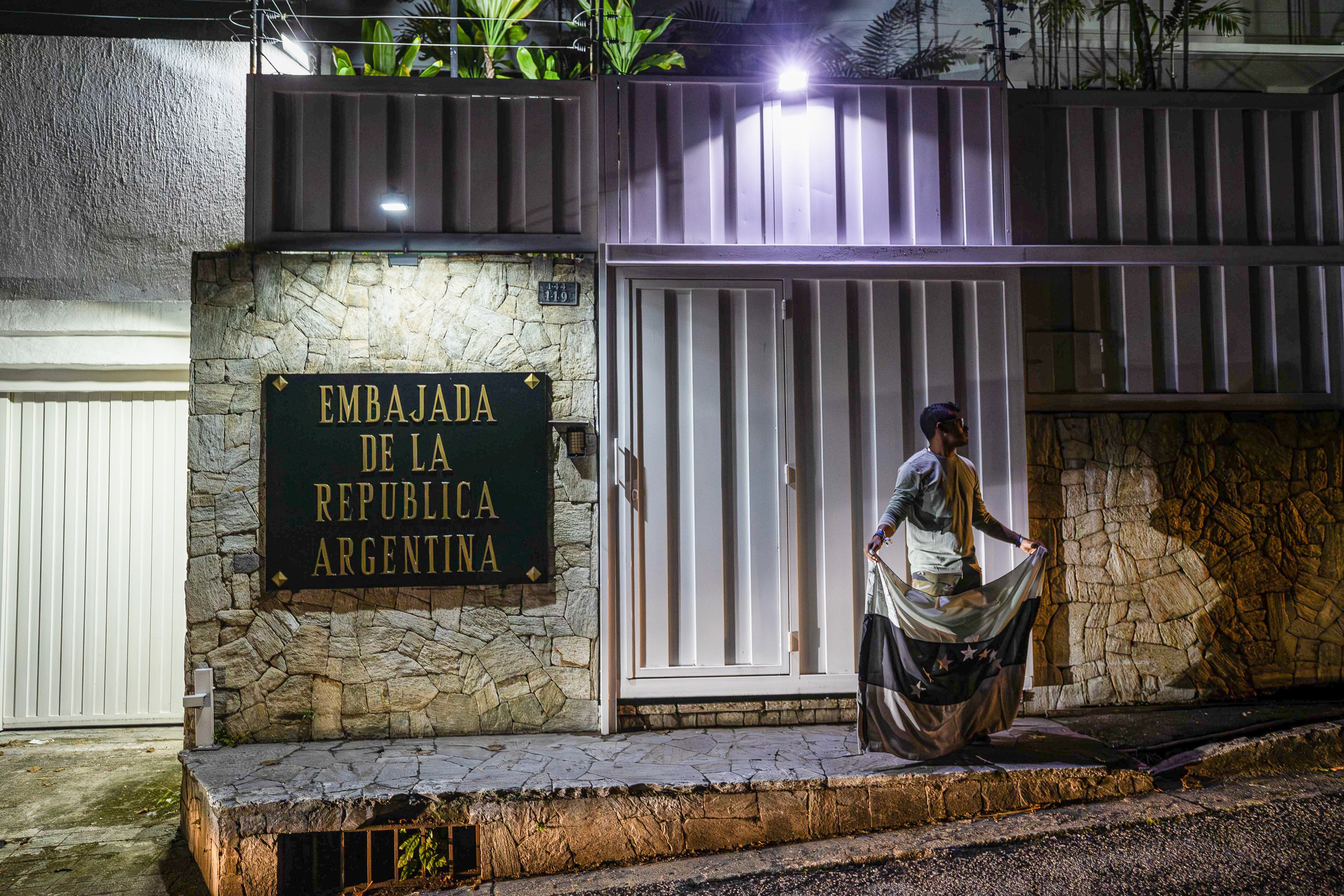 Una persona sostiene la bandera de Venezuela en color negro frente a la embajada de Argentina el en Caracas
