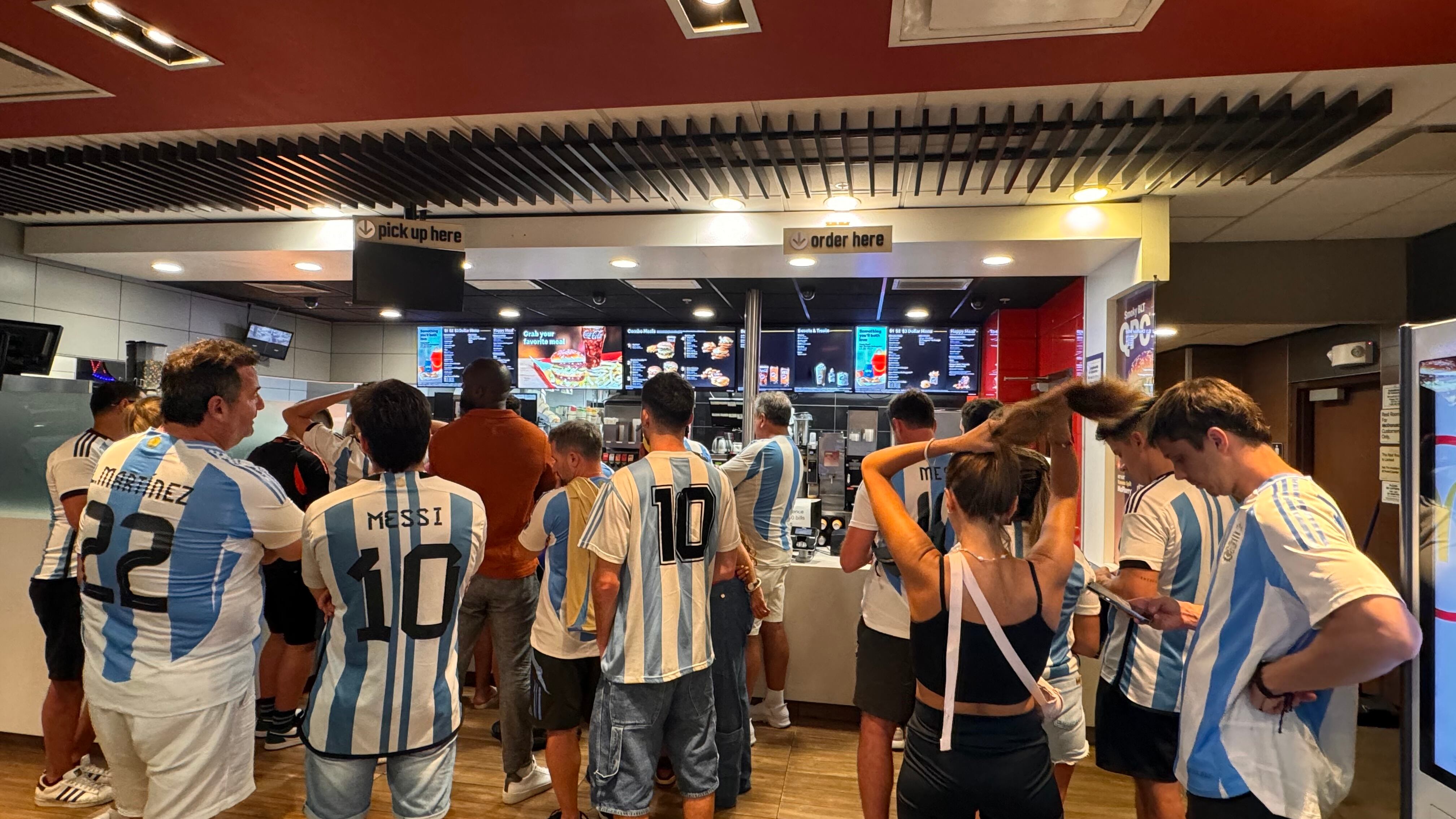 Una multitud de hinchas argentinos, vestidos con camisetas de la selección y agitando banderas celestes y blancas, celebra en las calles de Miami Beach durante la noche. La gente se muestra eufórica, tomando fotos y cantando, en una atmósfera festiva y llena de emoción tras la victoria de la Selección Argentina en la Copa América.