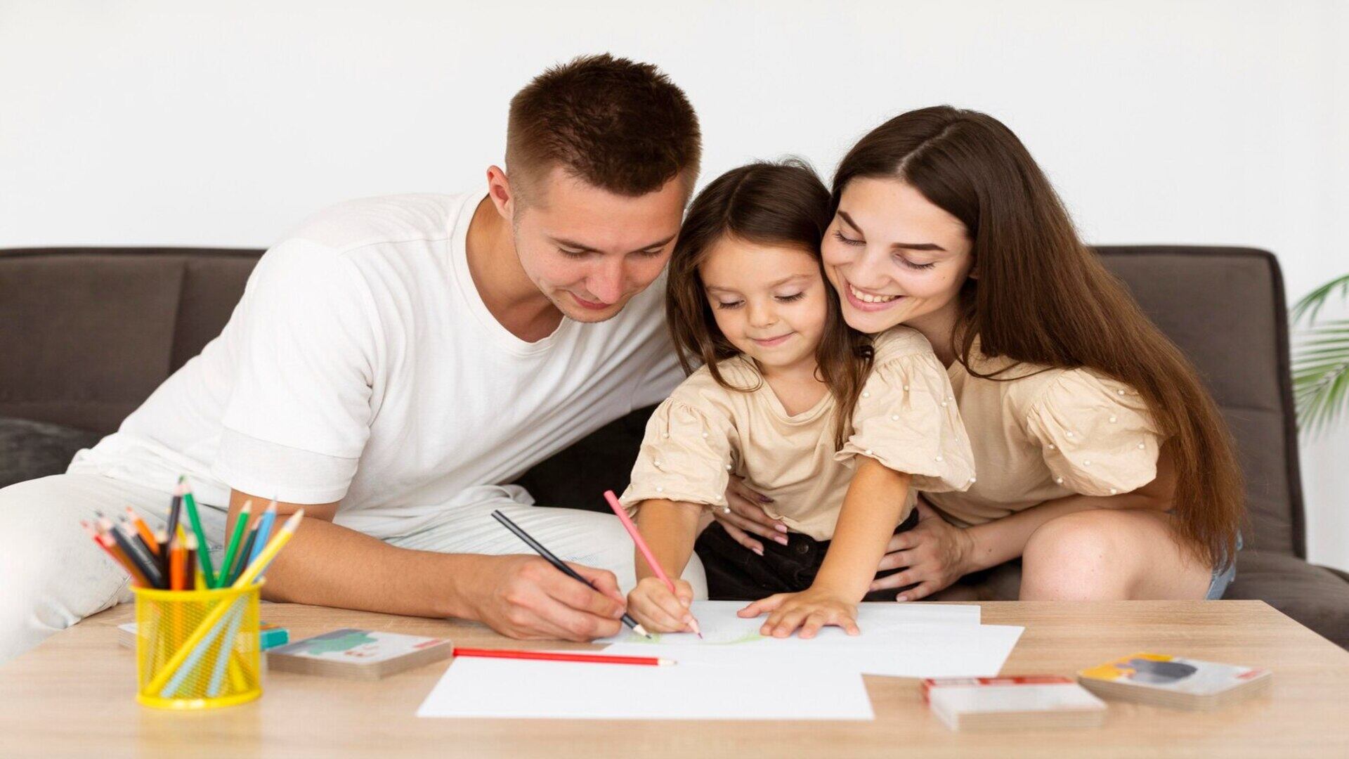 Mamá y papá haciendo la tarea con su hija pequeña (Freepik)