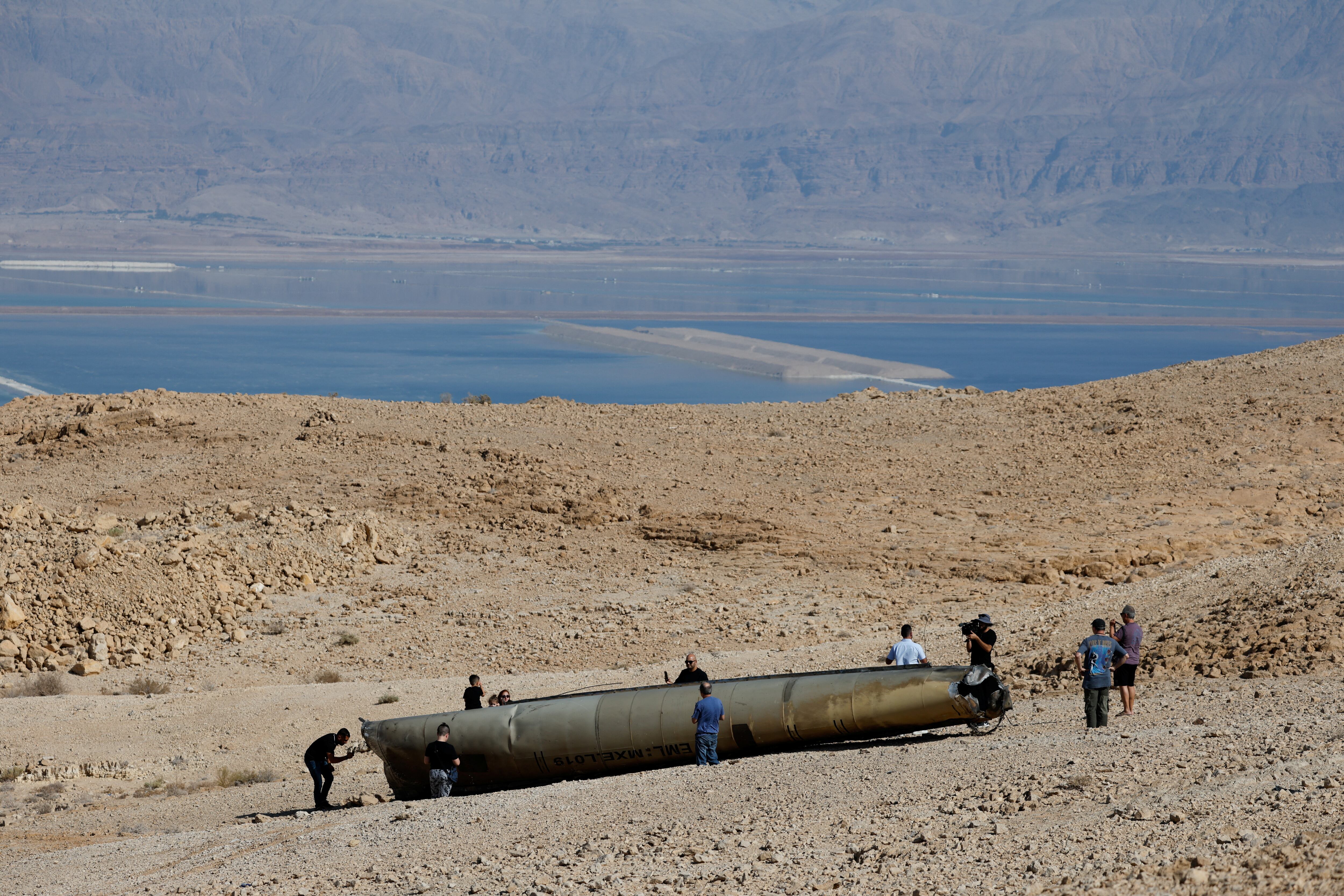 Varias personas se encuentran alrededor de los aparentes restos de un misil balístico que yacen en el desierto, luego de un ataque de Irán contra Israel, cerca de Arad