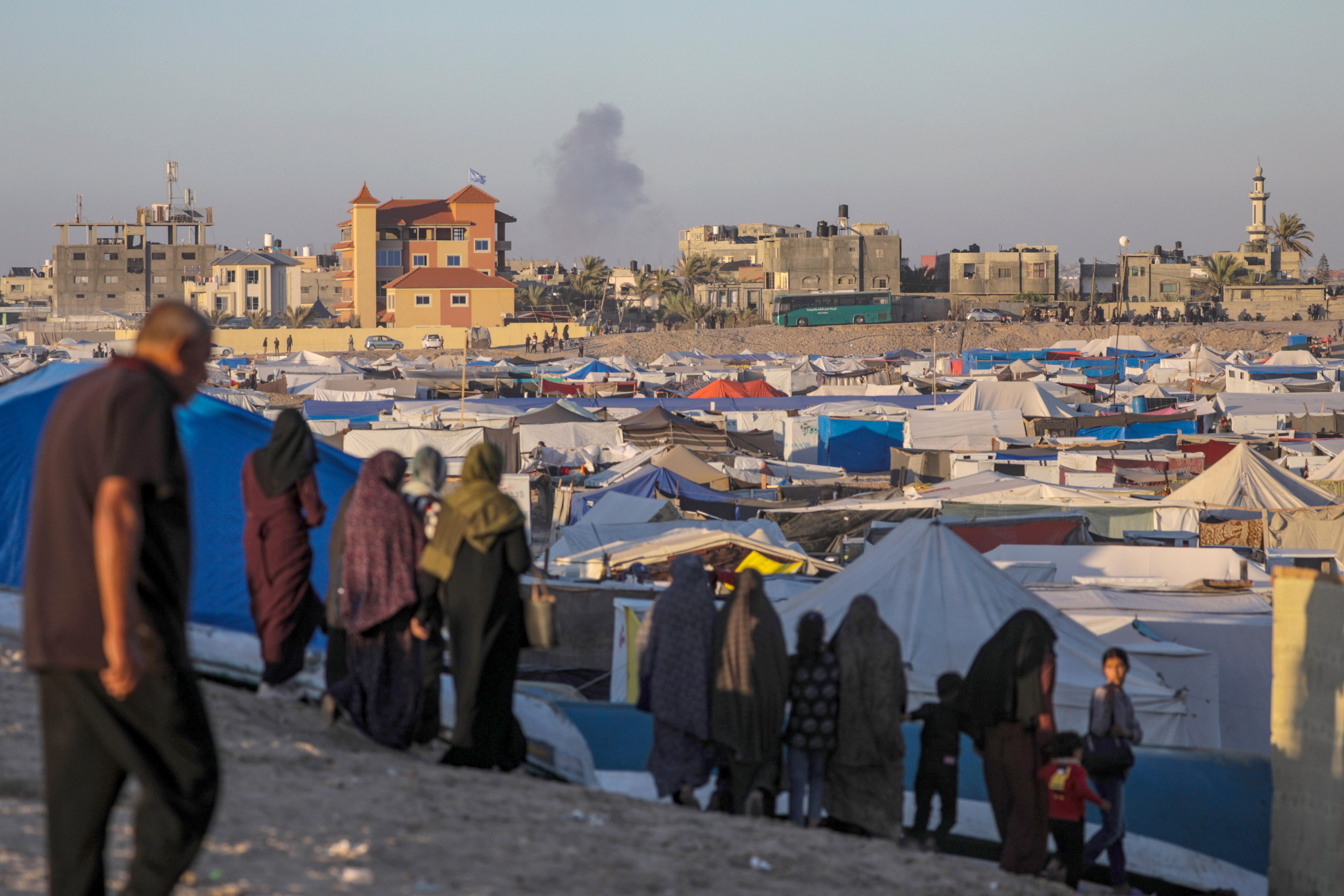 Palestinos desplazados internos en un campamento miran el humo que se eleva al fondo después de un ataque aéreo israelí, en Rafah  (EFE/EPA/MOHAMMED SABER)
