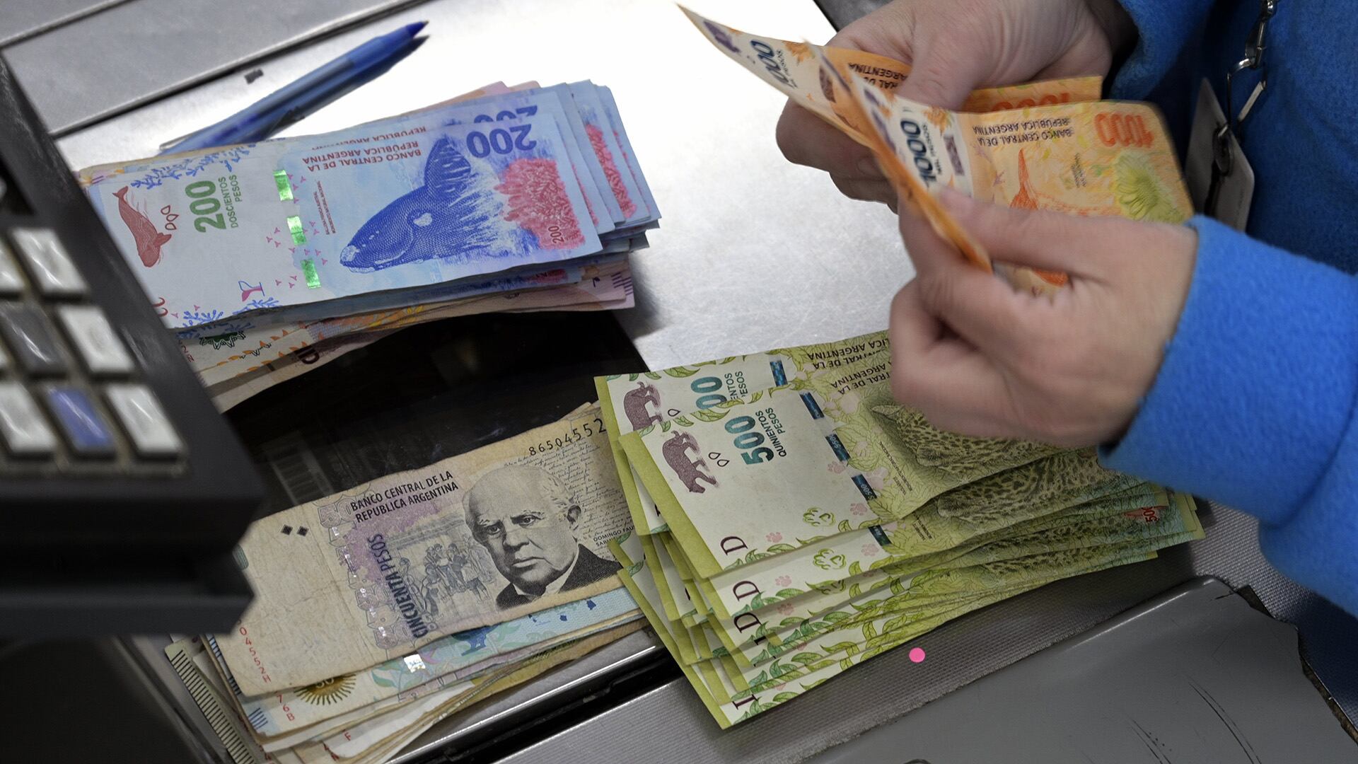 (FILES) In this file photo taken on August 15, 2019 a cashier counts Argentine pesos bills at a supermarket in Buenos Aires. - With unpaid credit cards, debts with the psicologyst and children's schools, middle class in Argentina is in crisis and in the border of default, as public accounts are. (Photo by JUAN MABROMATA / AFP)