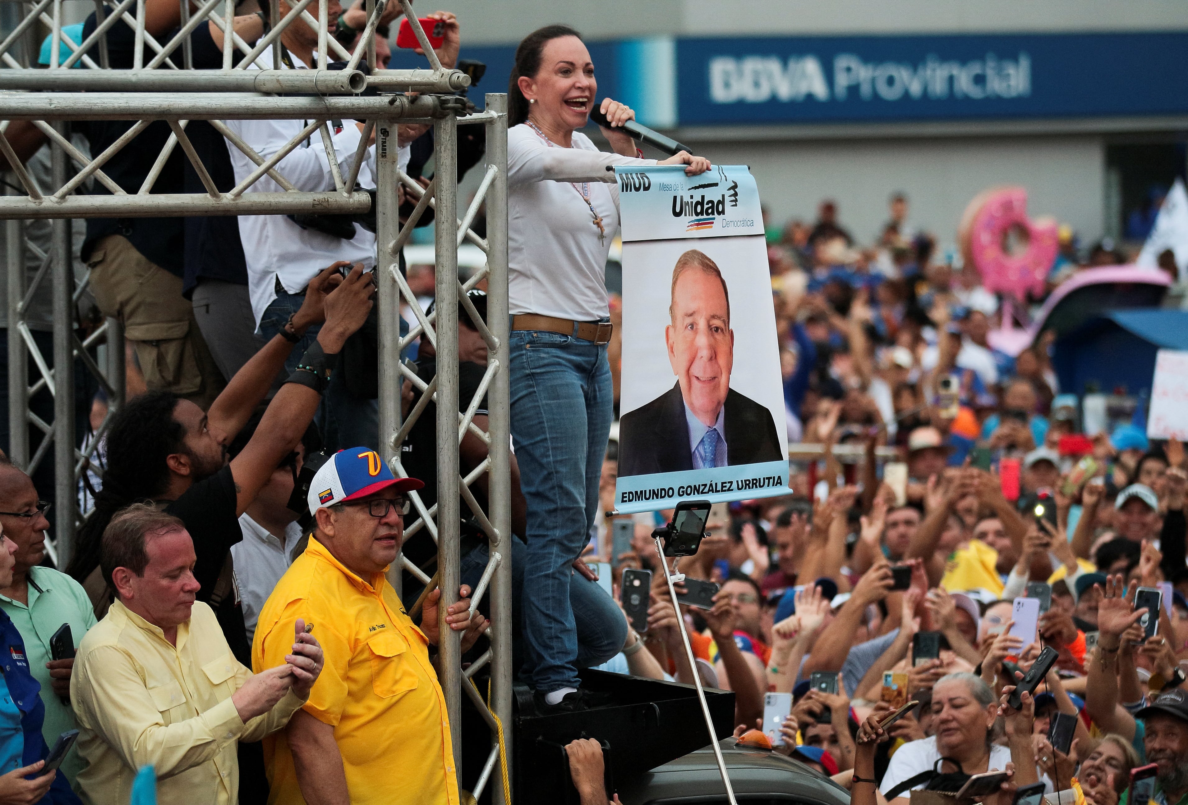 La líder opositora venezolana María Corina Machado se dirige a una multitud mientras sostiene una pancarta de campaña del candidato presidencial opositor Edmundo González Urrutia durante un mitin en Maracaibo (REUTERS/Isaac Urrutia)