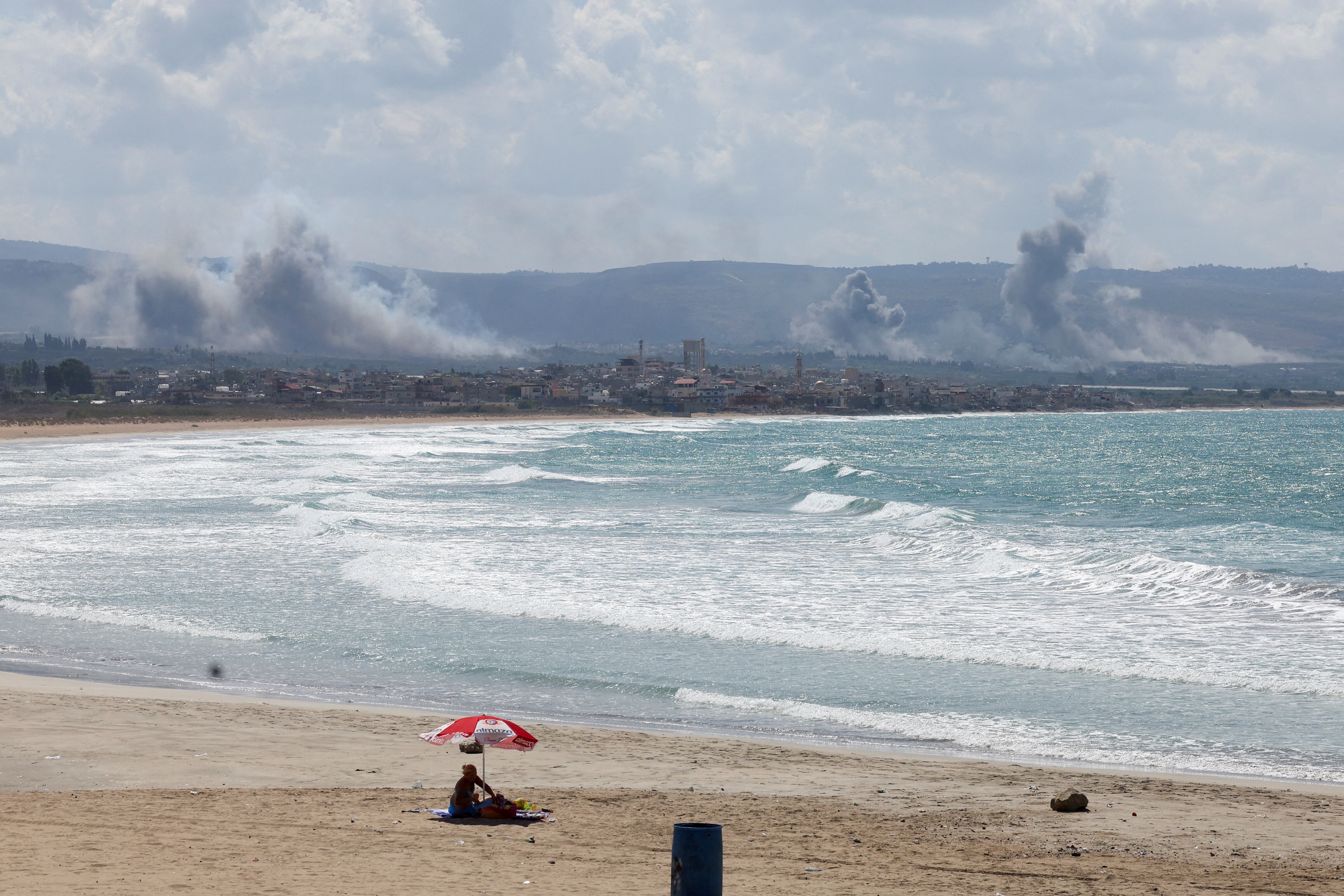 Una mujer sentada en una playa mientras el humo ondea sobre el sur del Líbano tras los ataques israelíes. (REUTERS/Aziz Taher)