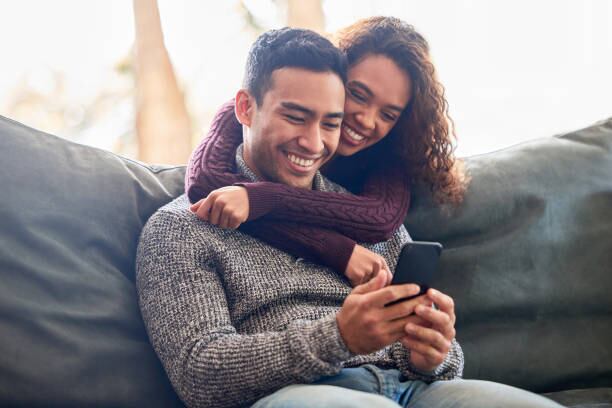 Un hombre sentado en un sillón mientras su pareja lo abraza por detrás y ambos sonríen (iStock)