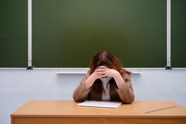 Una profesora con las manos en la cabeza sintiendo estrés en el aula de clases - Día del Maestro (Cecodap)