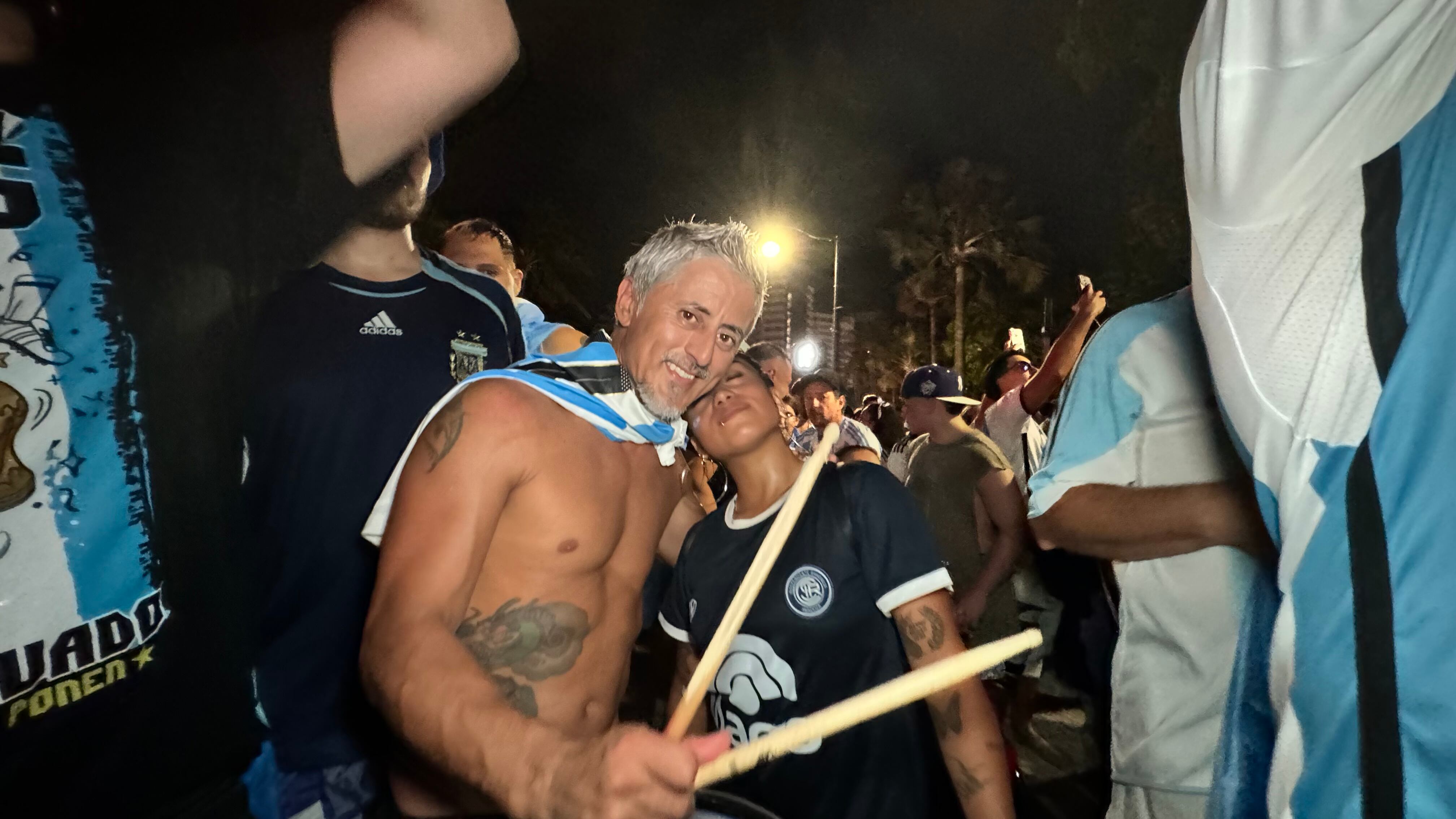 Una multitud de hinchas argentinos, vestidos con camisetas de la selección y agitando banderas celestes y blancas, celebra en las calles de Miami Beach durante la noche. La gente se muestra eufórica, tomando fotos y cantando, en una atmósfera festiva y llena de emoción tras la victoria de la Selección Argentina en la Copa América.