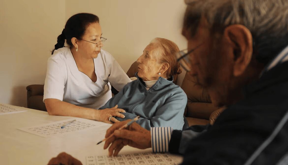 Una mujer atiende a una adulta mayor que está sentada al lado de un anciano - Alzheimer (El Universo)