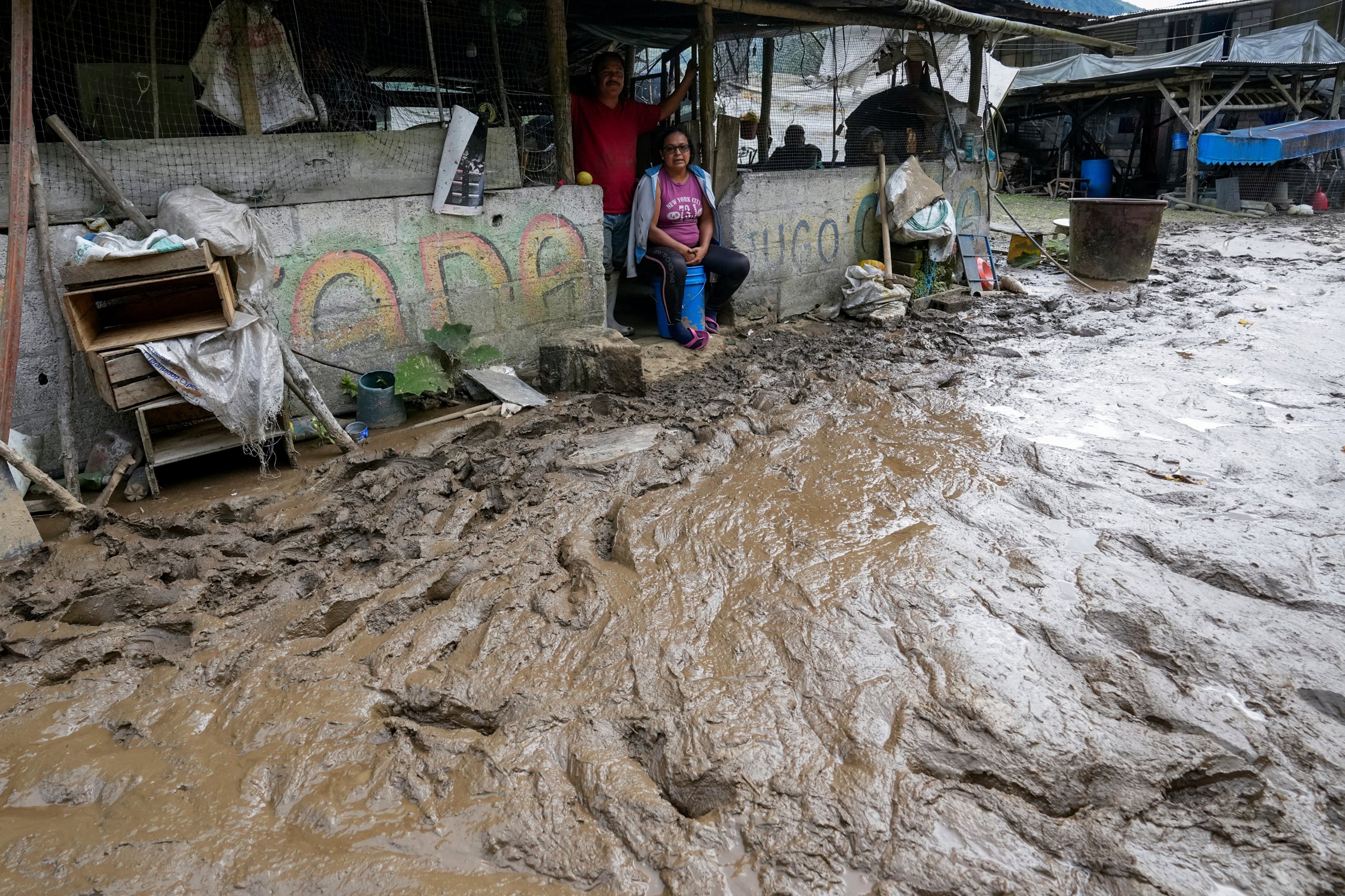 Varios residentes en sus casas ante una vía anegada de barro tras el deslizamiento de tierra provocado por las fuertes lluvias en Baños de Agua Santa, Ecuador, el lunes 17 de junio de 2024. (AP Foto/Dolores Ochoa)