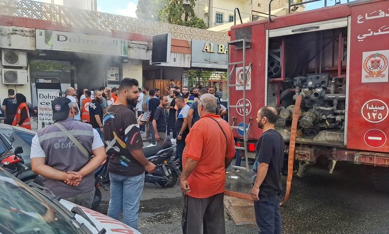 Varias personas se reúnen mientras sale humo de una tienda de móviles en Sidón, Líbano (REUTERS/Hassan Hankir)