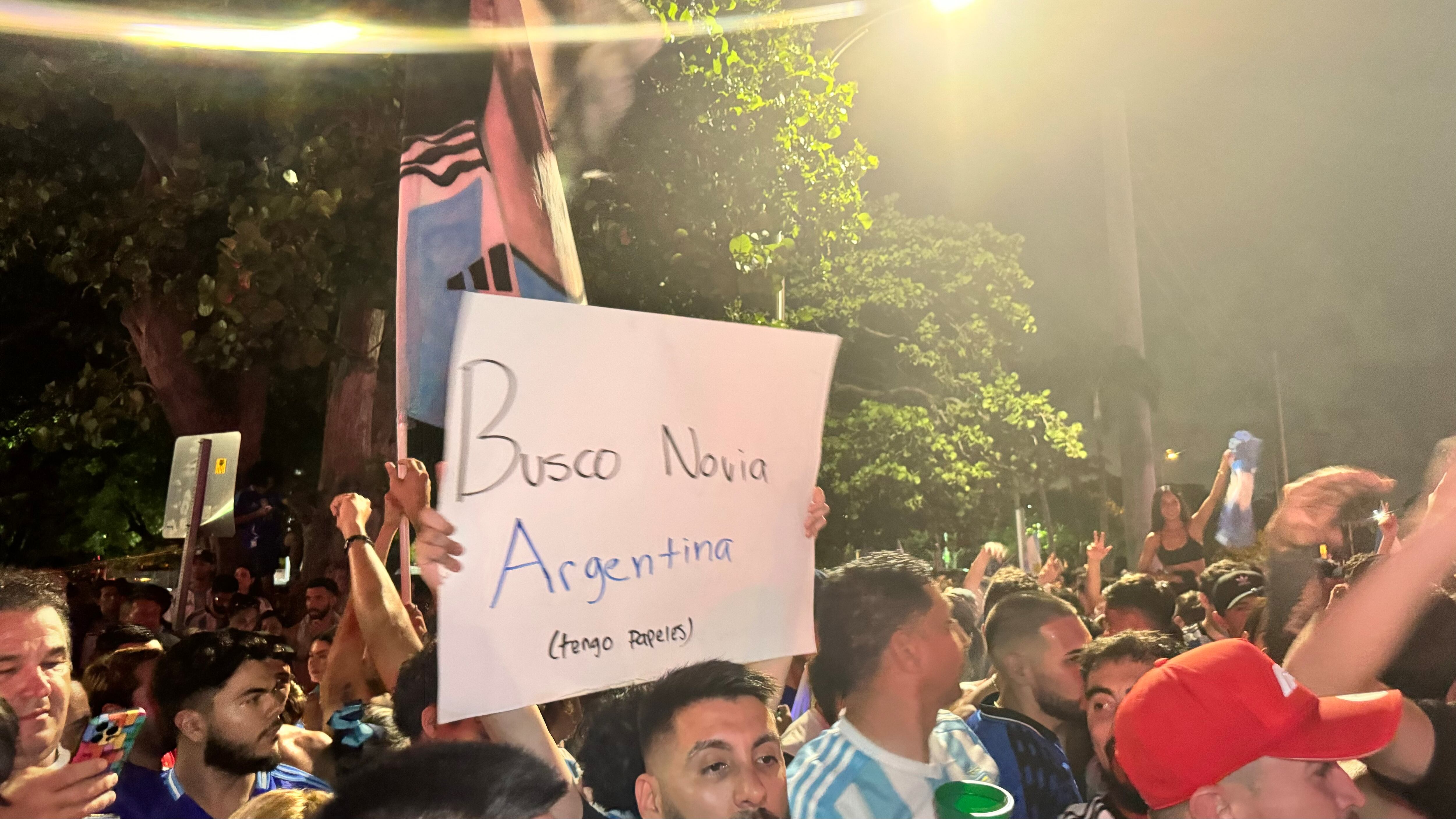 Una multitud de hinchas argentinos, vestidos con camisetas de la selección y agitando banderas celestes y blancas, celebra en las calles de Miami Beach durante la noche. La gente se muestra eufórica, tomando fotos y cantando, en una atmósfera festiva y llena de emoción tras la victoria de la Selección Argentina en la Copa América.