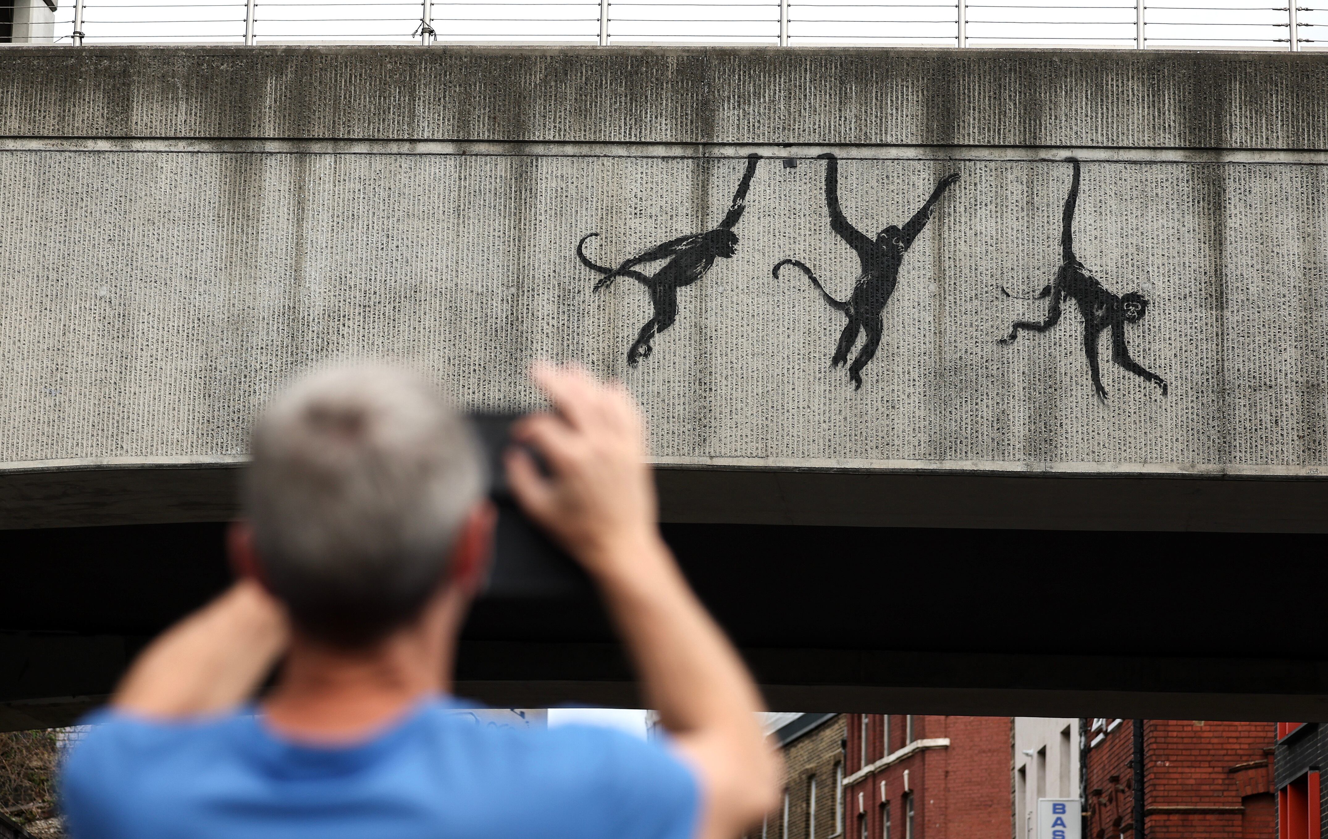 Un hombre toma fotografías de la obra de arte de Banksy que presenta monos en el costado de un puente ferroviario en Shoreditch, al este de Londres (Foto: EFE/EPA/Andy Lluvia) 
