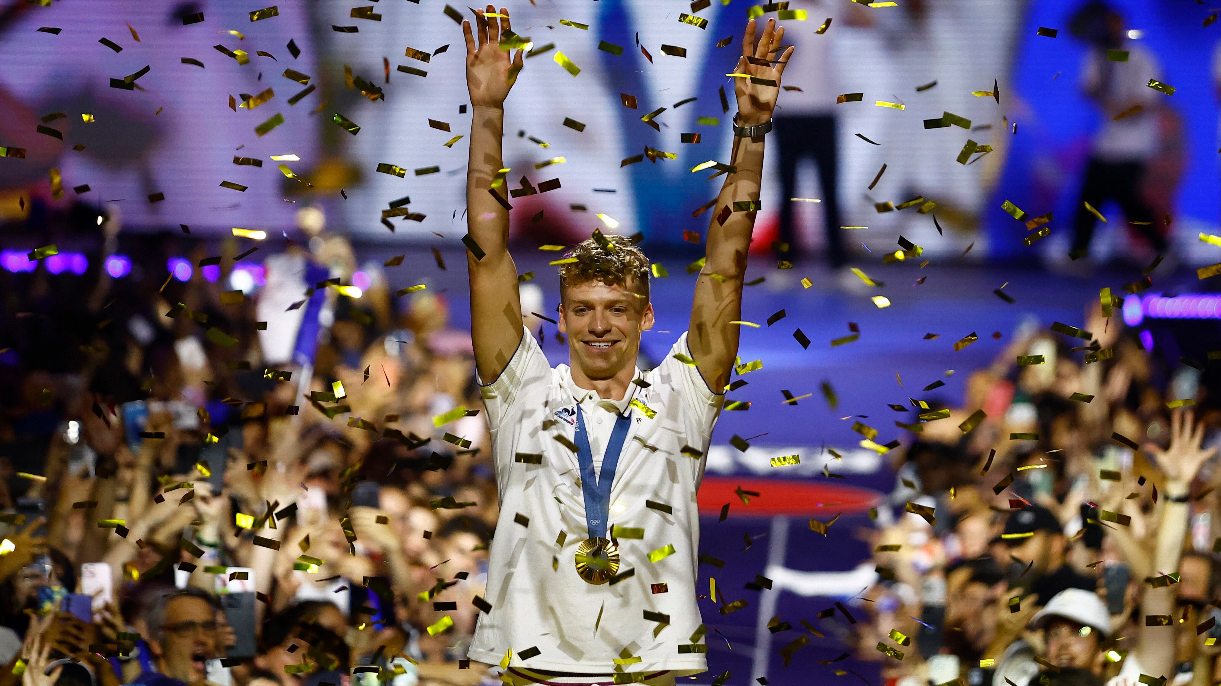 Paris 2024 Olympics - Swimming - Paris, France - August 5, 2024 Leon Marchand of France raises his arms above his head as gold ticker tape falls at Club France. REUTERS/Abdul Saboor