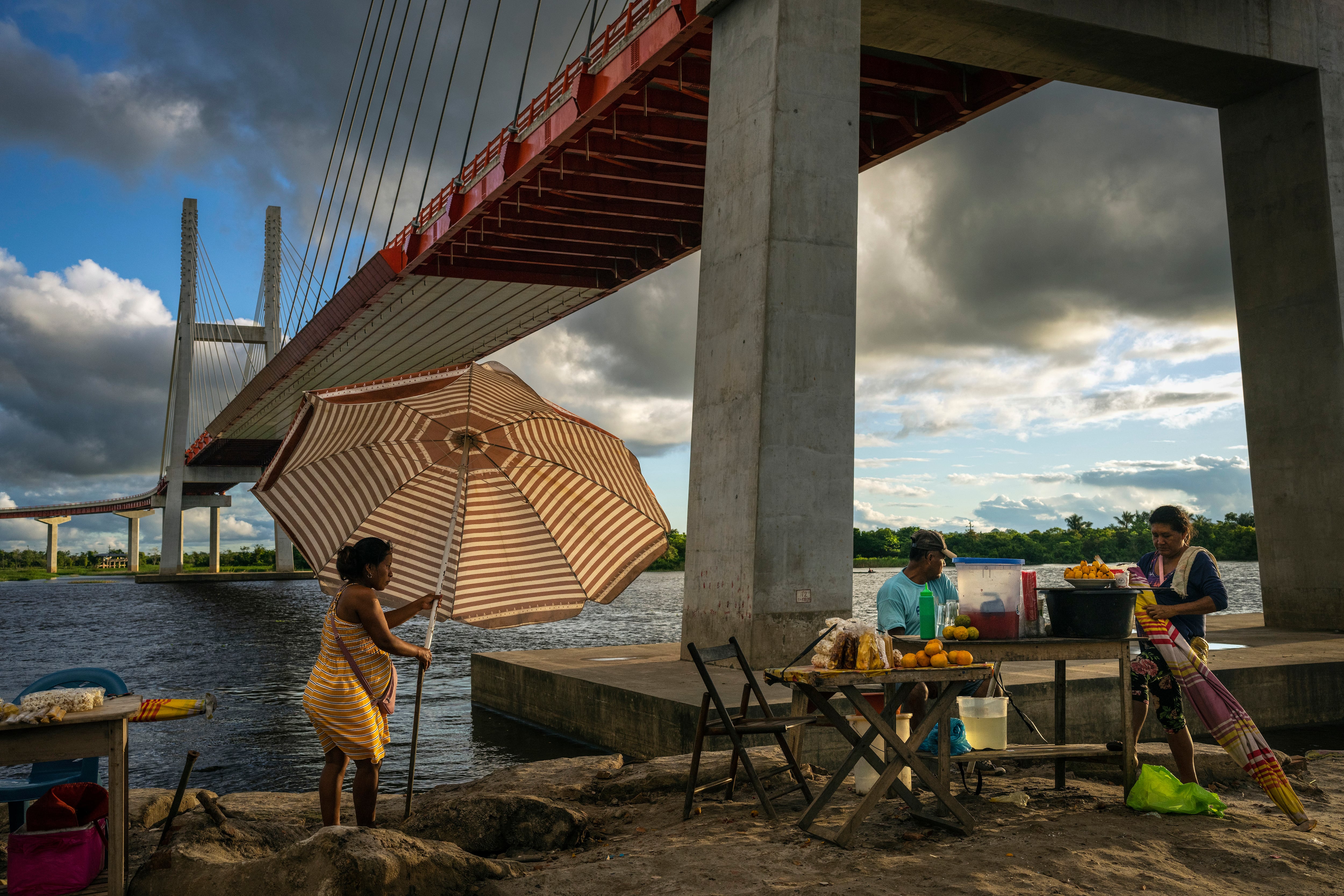 Vendedores colocan puestos de comida bajo un puente que forma parte de un proyecto federal de carreteras que pasa sobre el río Nanay, en Iquitos, Perú, el lunes 27 de mayo de 2024. (AP Foto/Rodrigo Abd)