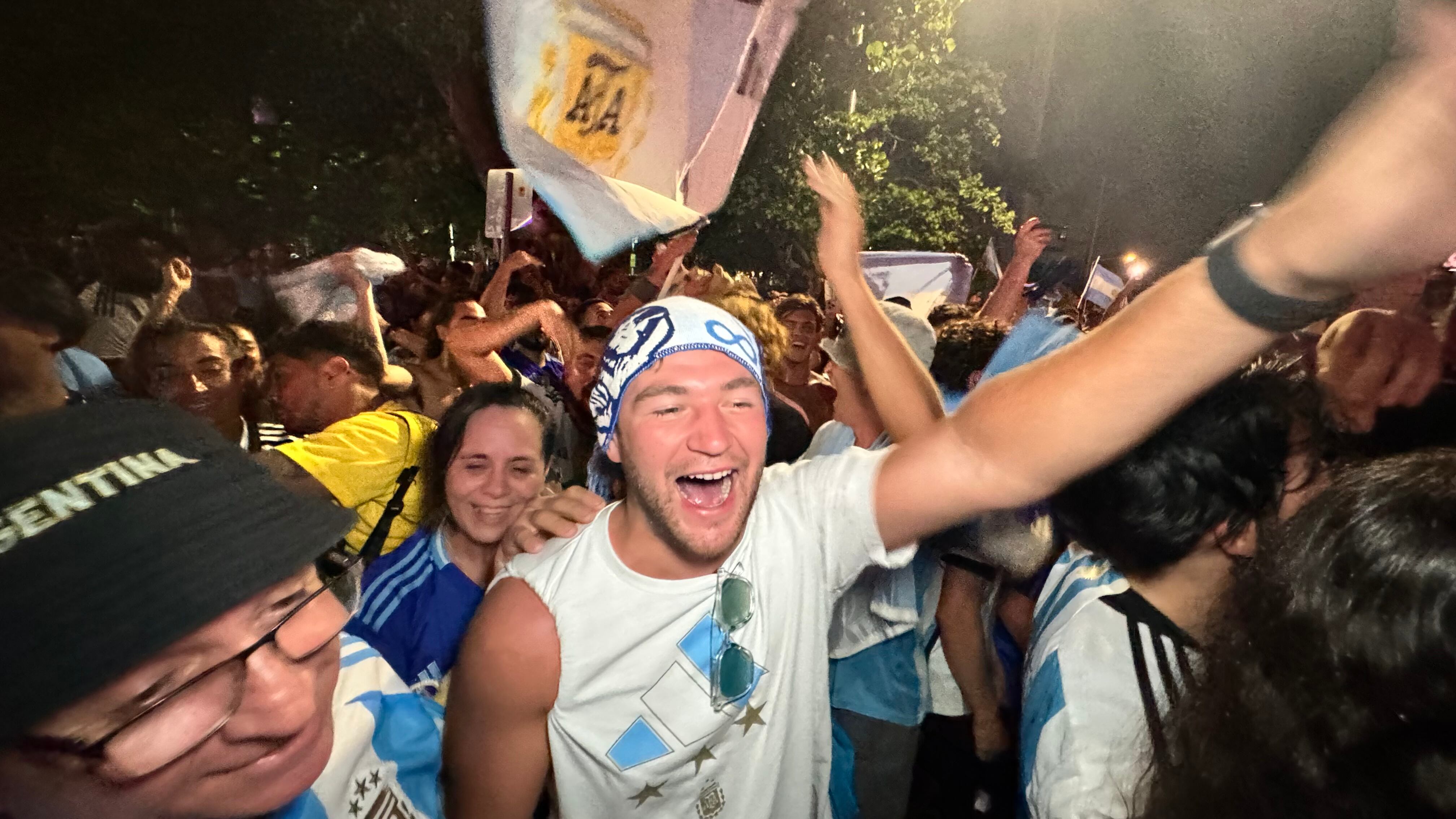 Una multitud de hinchas argentinos, vestidos con camisetas de la selección y agitando banderas celestes y blancas, celebra en las calles de Miami Beach durante la noche. La gente se muestra eufórica, tomando fotos y cantando, en una atmósfera festiva y llena de emoción tras la victoria de la Selección Argentina en la Copa América.