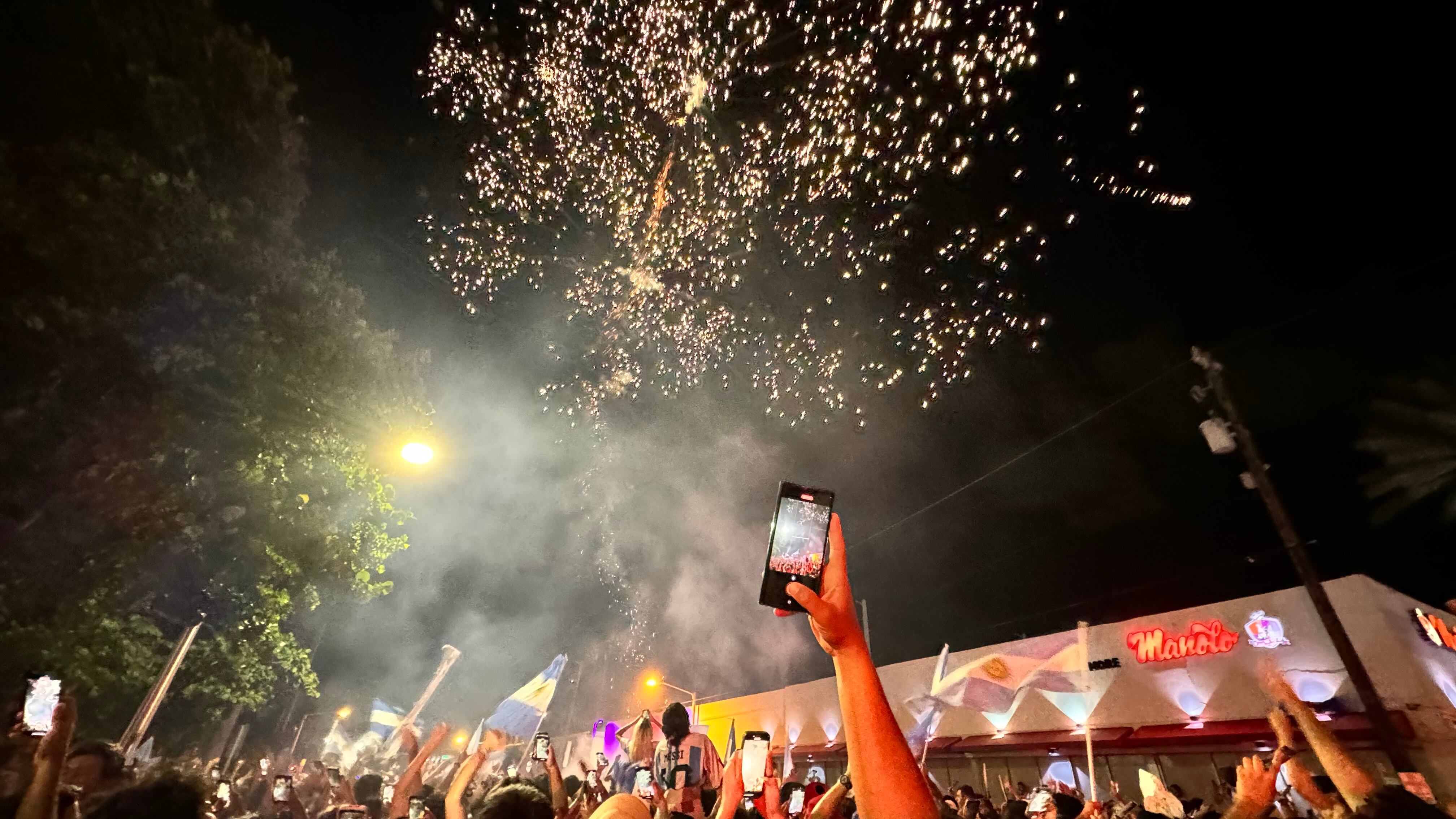 Una multitud de hinchas argentinos, vestidos con camisetas de la selección y agitando banderas celestes y blancas, celebra en las calles de Miami Beach durante la noche. La gente se muestra eufórica, tomando fotos y cantando, en una atmósfera festiva y llena de emoción tras la victoria de la Selección Argentina en la Copa América.