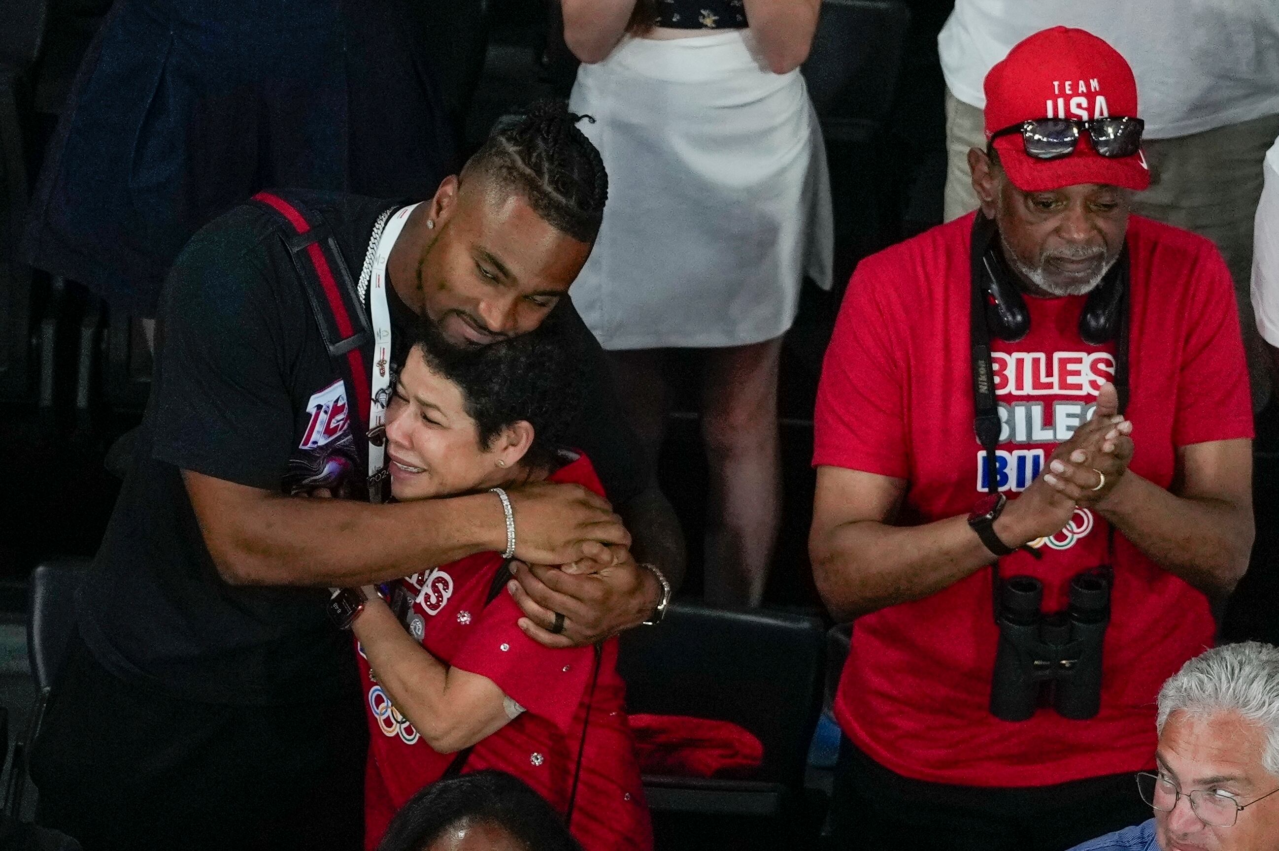 Jonathan Owens, esposo de la gimnasta de los Estados Unidos, Simone Biles, abraza a su madre adoptiva Nellie Biles, mientras es condecorada con la medalla de oro durante las finales del all-around de la Gimnasia Artística Femenina, en el Bercy Arena, en París, Francia. A su lado, Ronald, abuelo de la atleta y su padre adoptivo (AP Foto/Morry Gash)