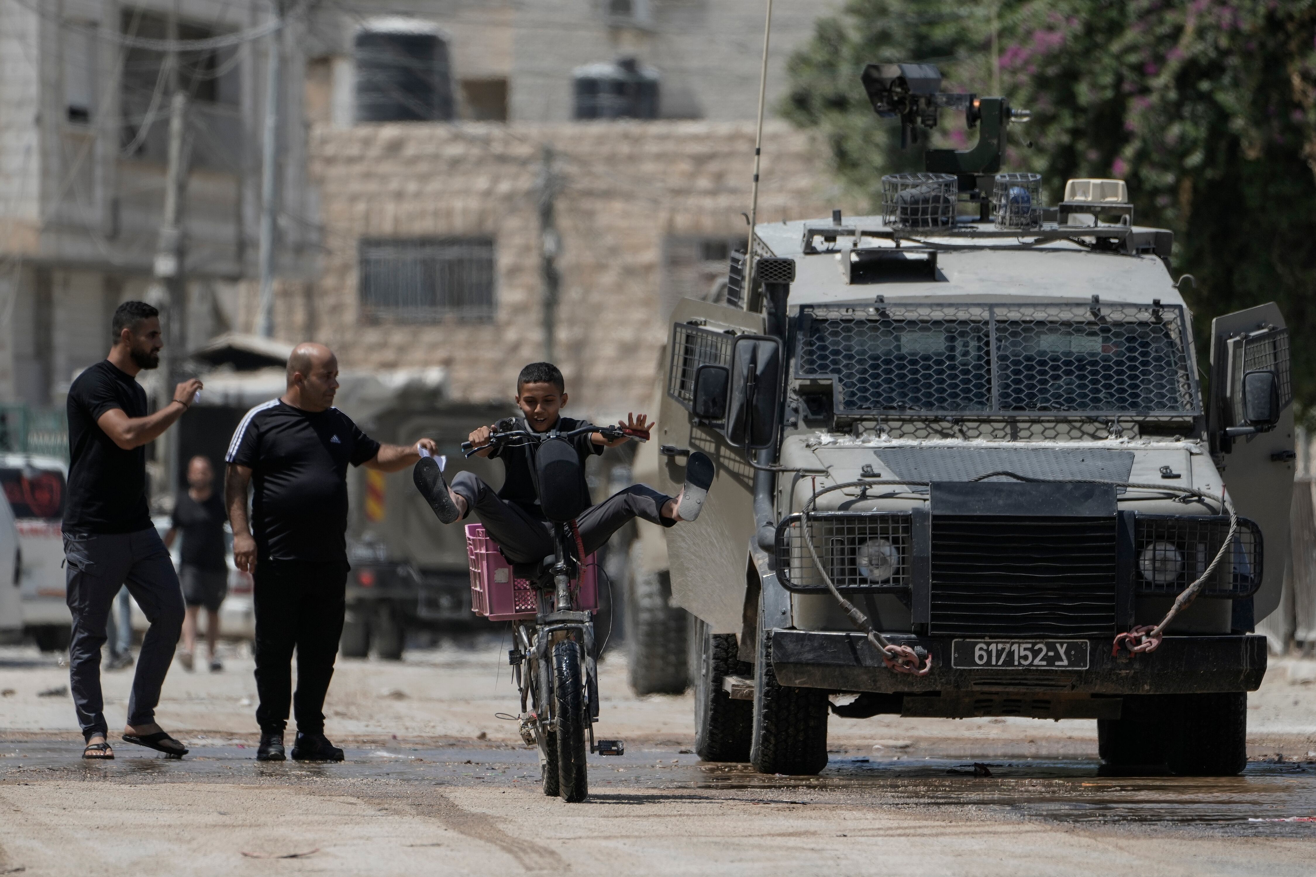 Un niño pasa en bicicleta junto a un vehículo blindado durante una operación militar en la ciudad cisjordana de Yenín  (AP Foto/Majdi Mohammed)