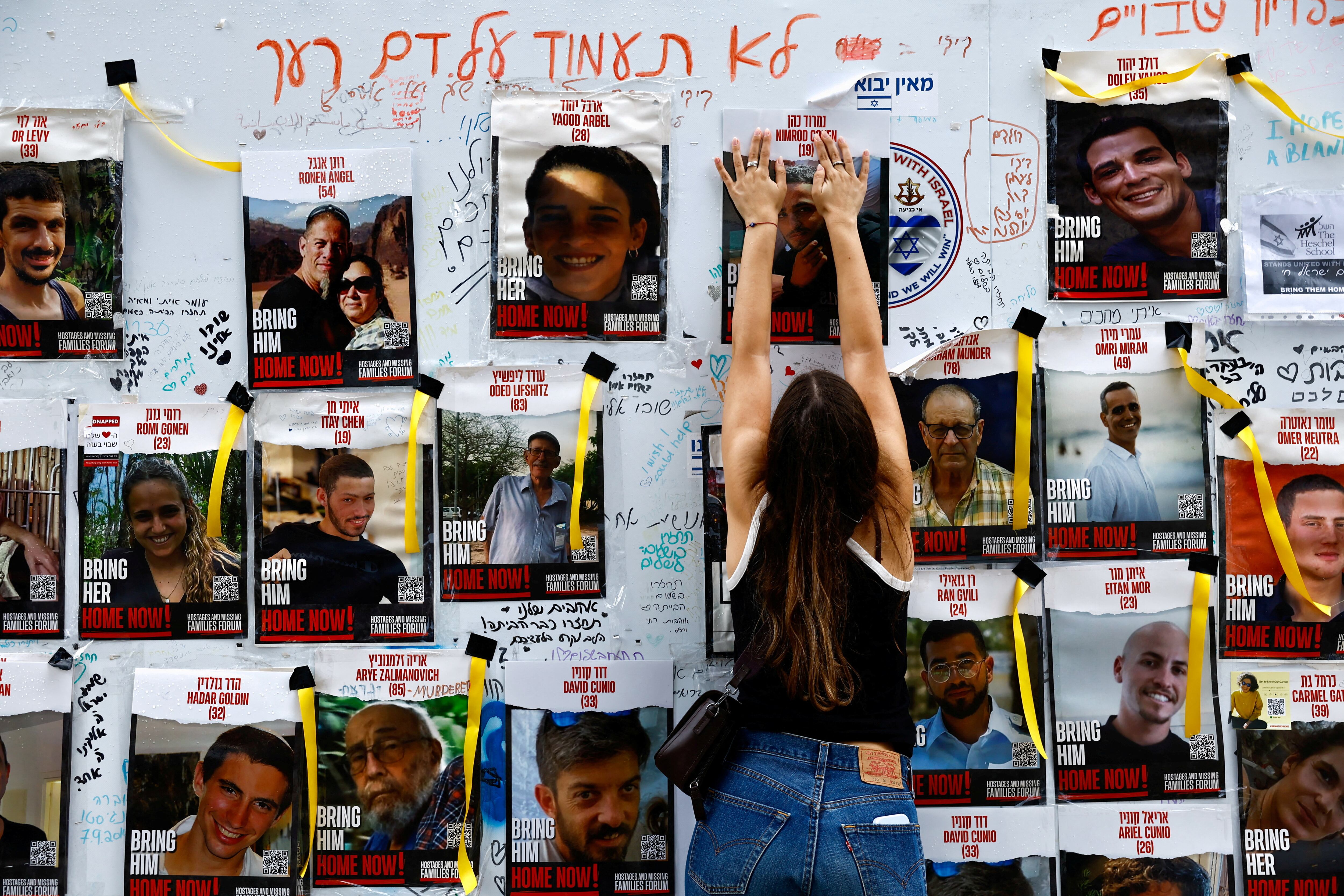 Una mujer cuelga un cartel en un tablón de anuncios en Tel Aviv con imágenes de personas secuestradas por Hamas el 7 de octubre de 2023