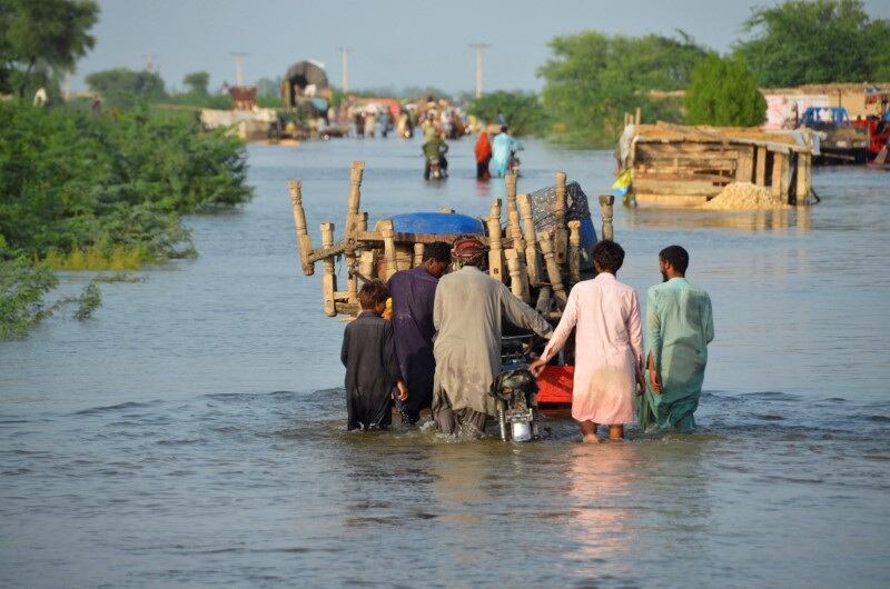 Varios hombres caminan por una carretera inundada con sus pertenencias, tras las lluvias e inundaciones registradas durante la estación monzónica en Sohbatpur, Pakistán. 28 de agosto de 2022 (REUTERS/Amer Hussain)