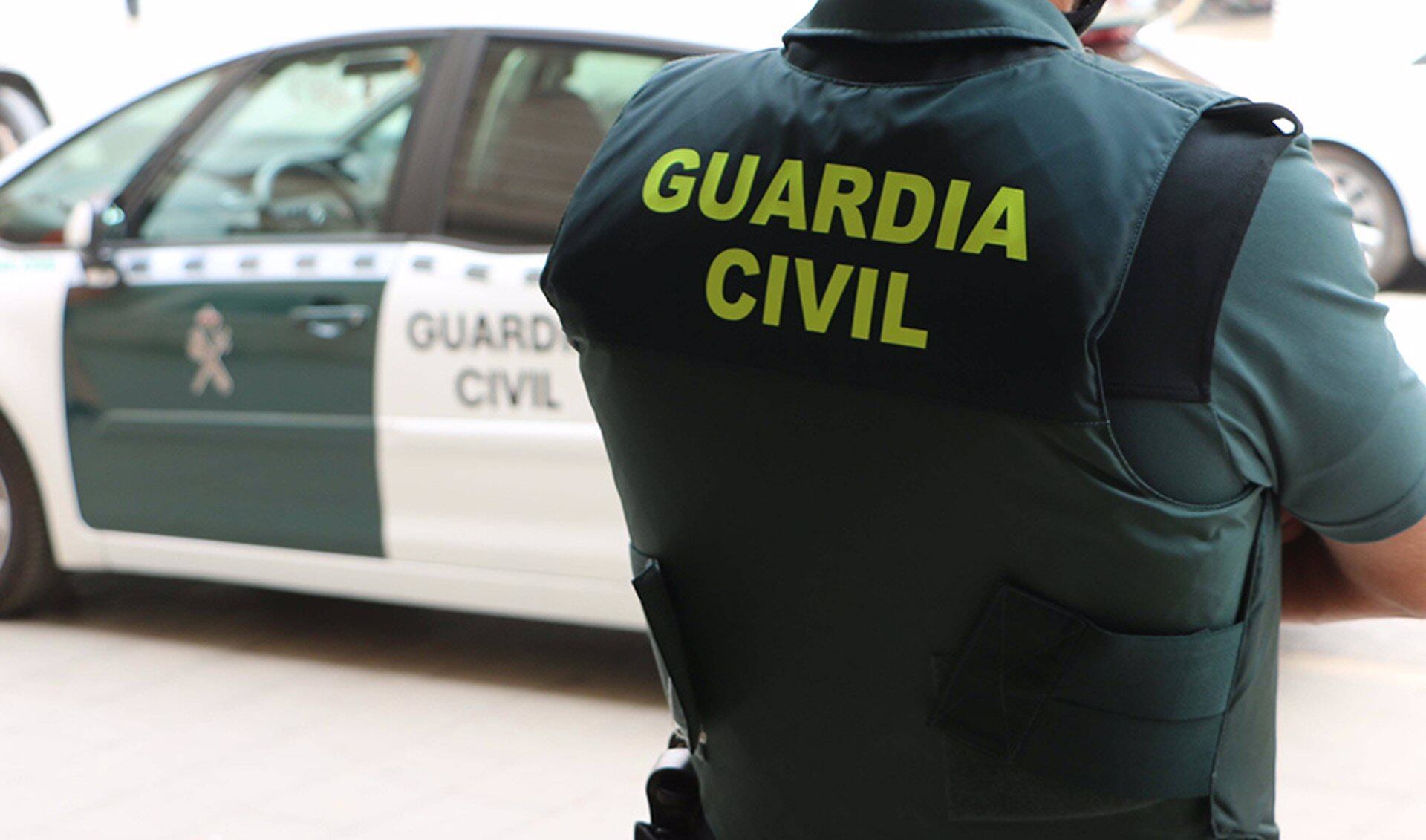 Un agente de la Guardia Civil, de espaldas, junto a un vehículo oficial.

