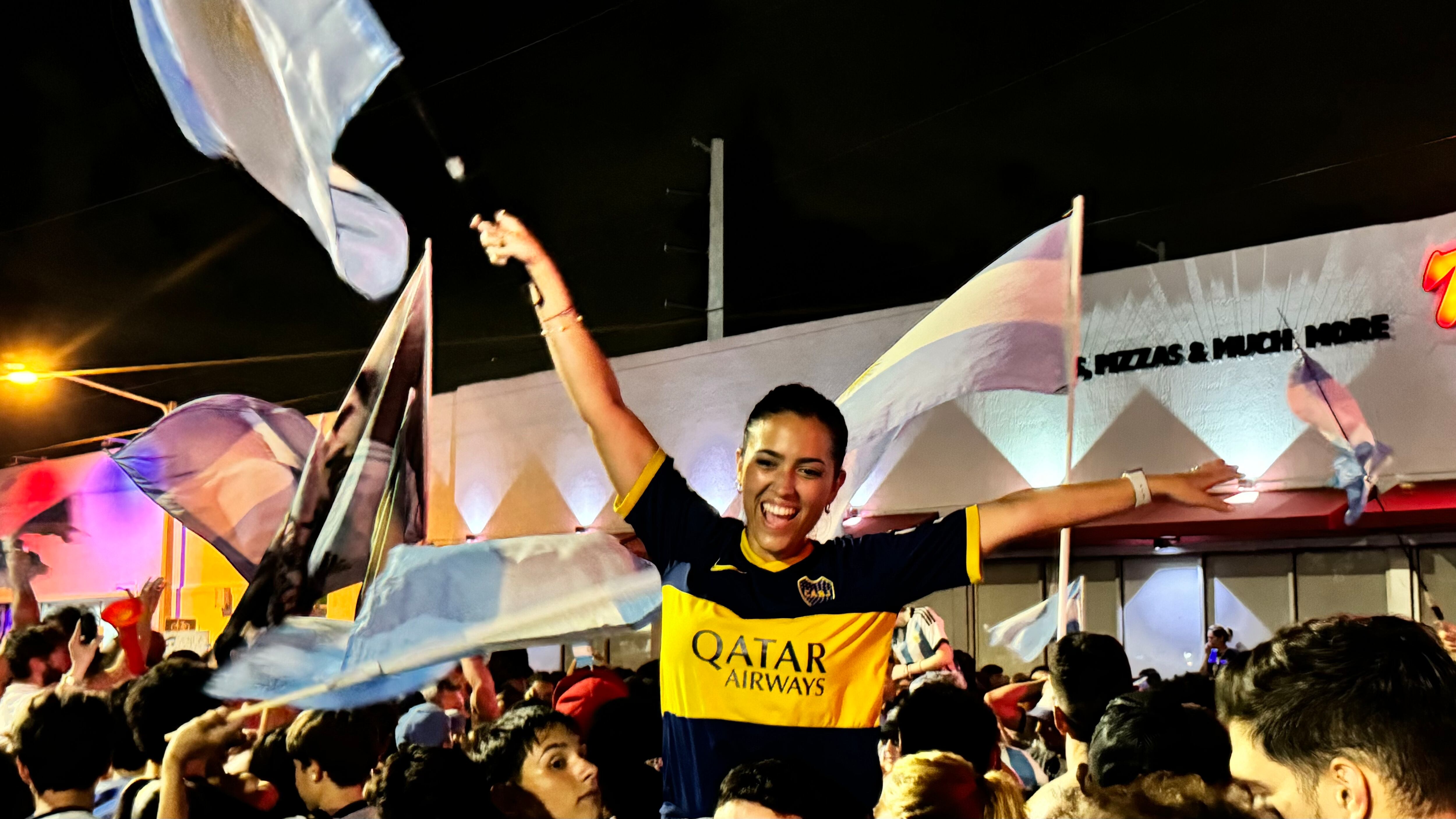 Una multitud de hinchas argentinos, vestidos con camisetas de la selección y agitando banderas celestes y blancas, celebra en las calles de Miami Beach durante la noche. La gente se muestra eufórica, tomando fotos y cantando, en una atmósfera festiva y llena de emoción tras la victoria de la Selección Argentina en la Copa América.