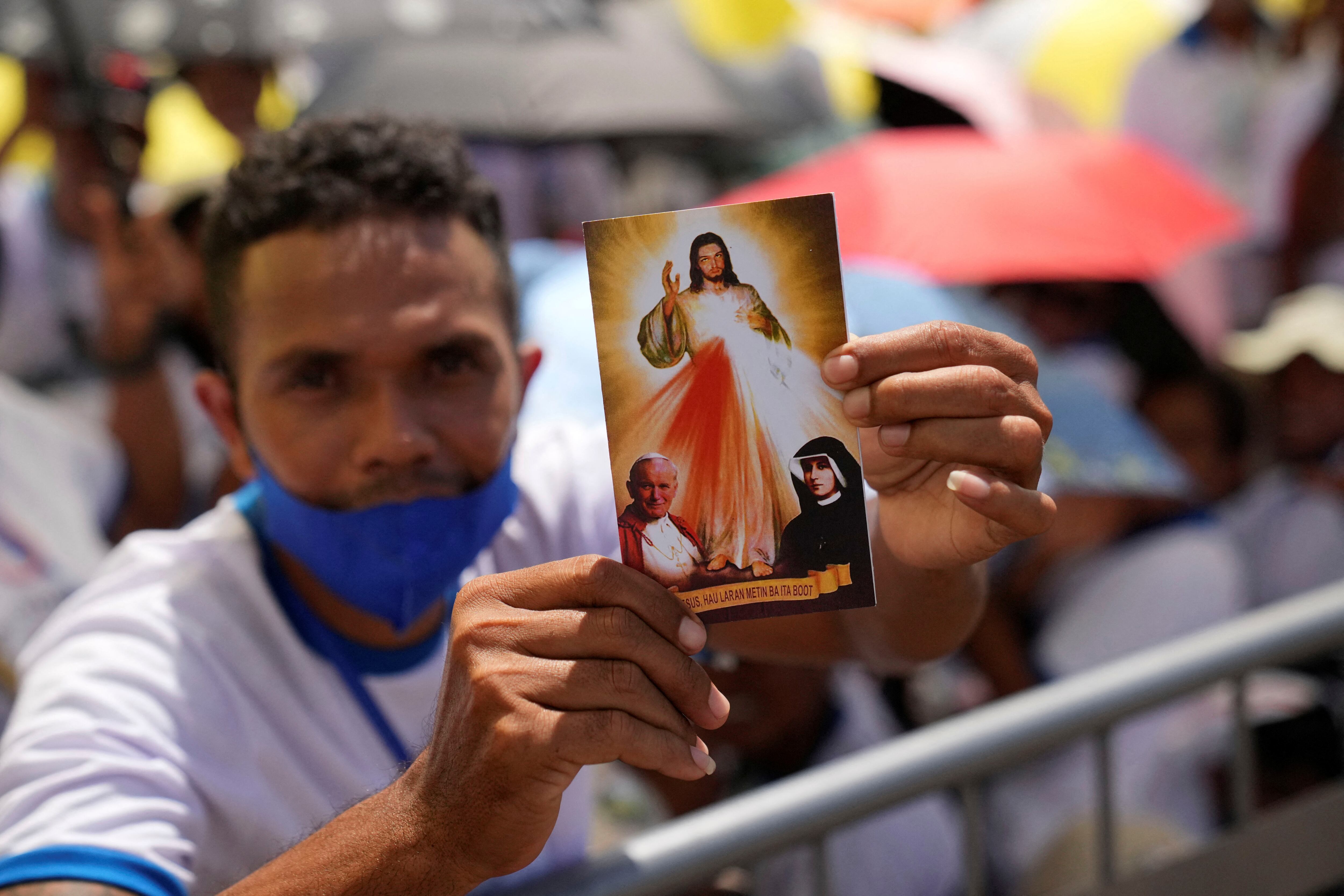 Un fiel sostiene una postal mientras espera en el parque de Tacitolu la misa del Papa Francisco en Dili.