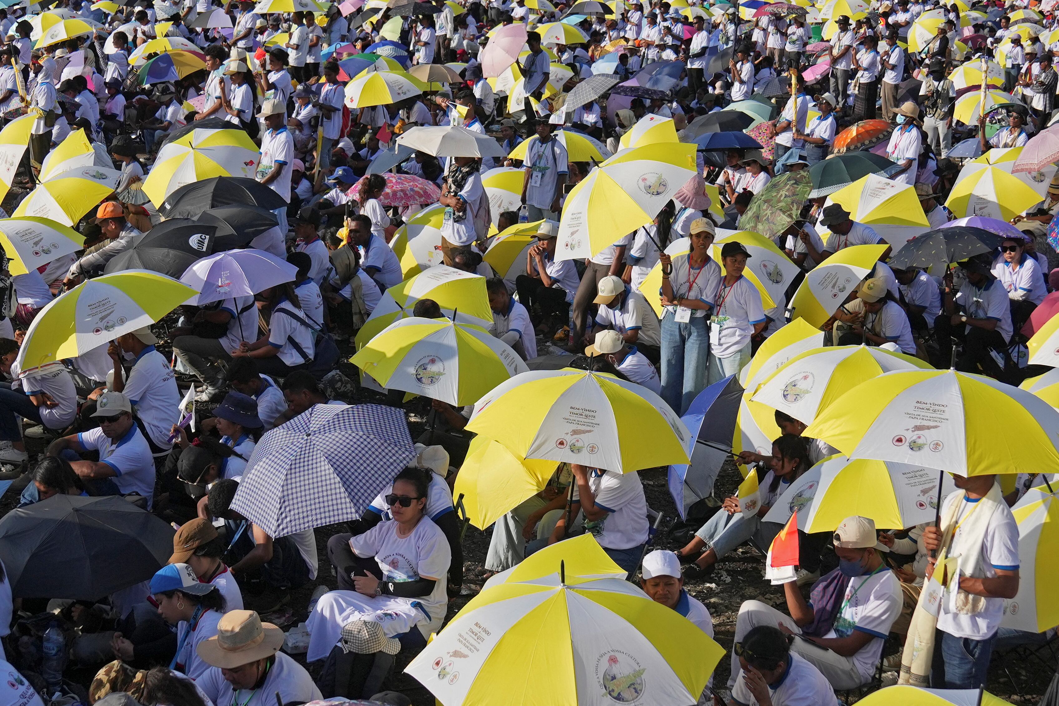 Personas congregadas con paraguas de color blanco y amarillo, en representación de la bandera del Vaticano.