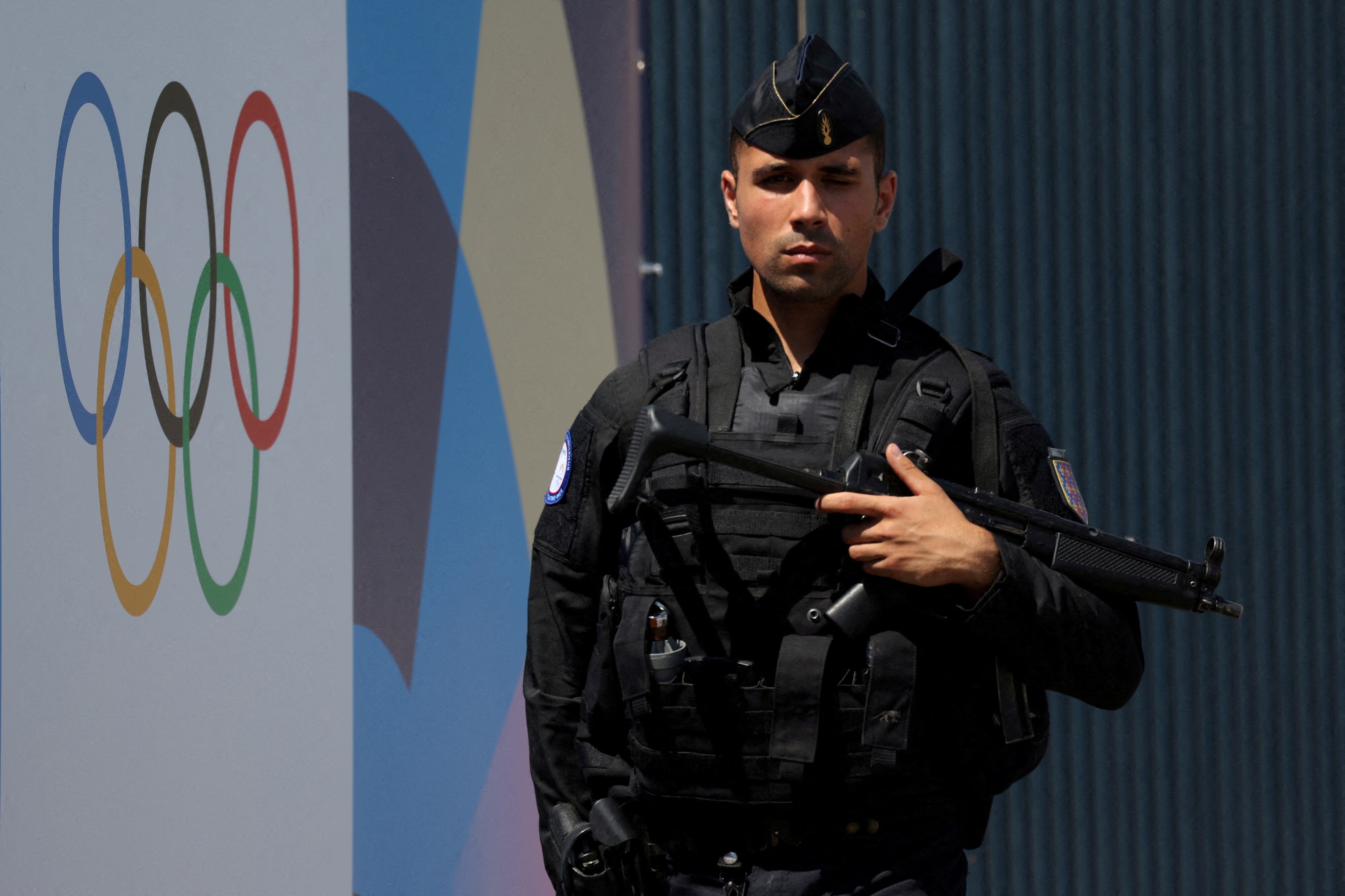 Un gendarme francés pasa junto a un cartel con los aros olímpicos cerca de la Asamblea Nacional mientras se despliega el perímetro de seguridad para la ceremonia de apertura antes de los Juegos Olímpicos de París 2024 (REUTERS/Kevin Coombs/File Photo)