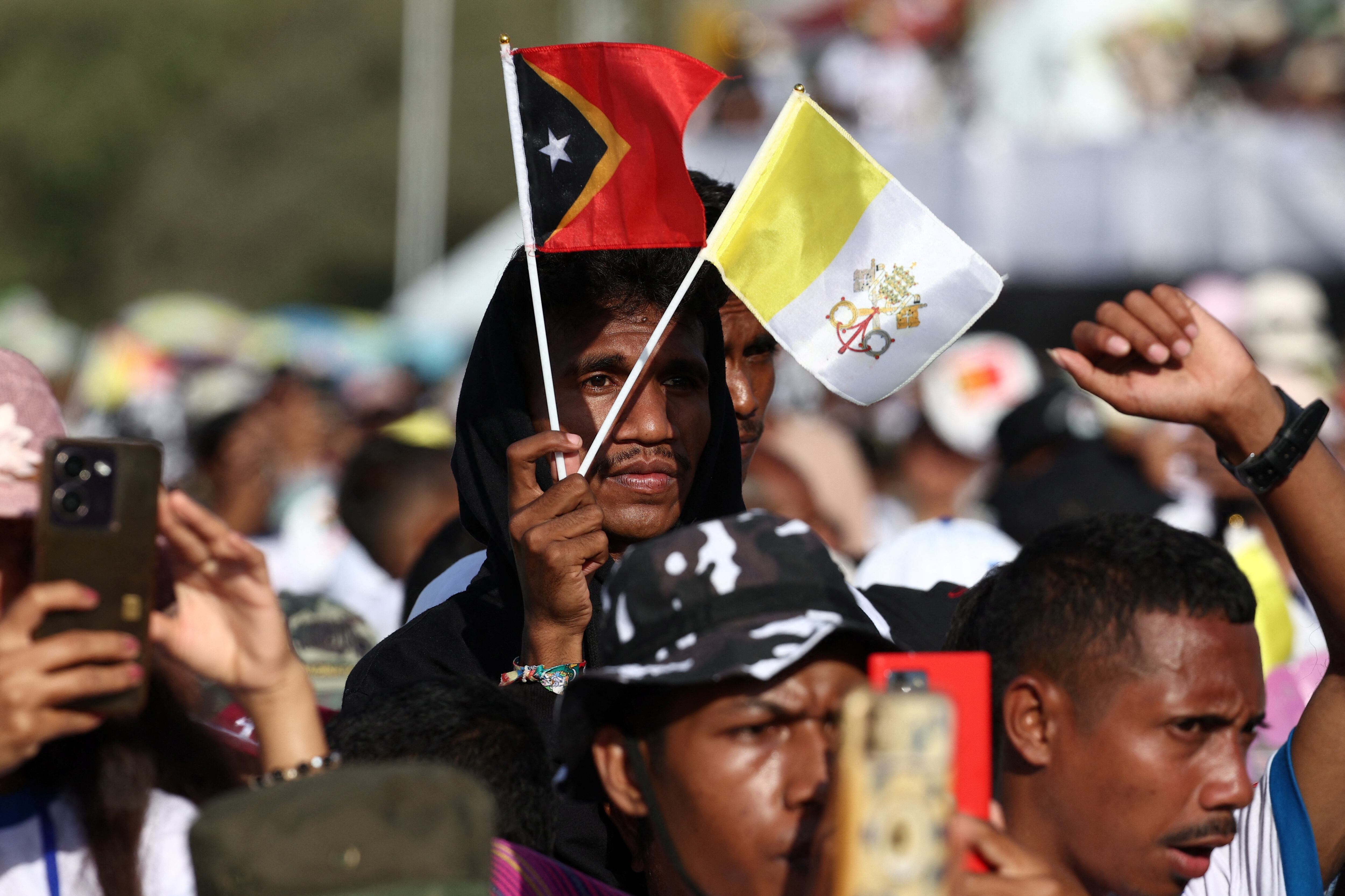 Un hombre sostiene una bandera de Timor Oriental y otra del Vaticano.