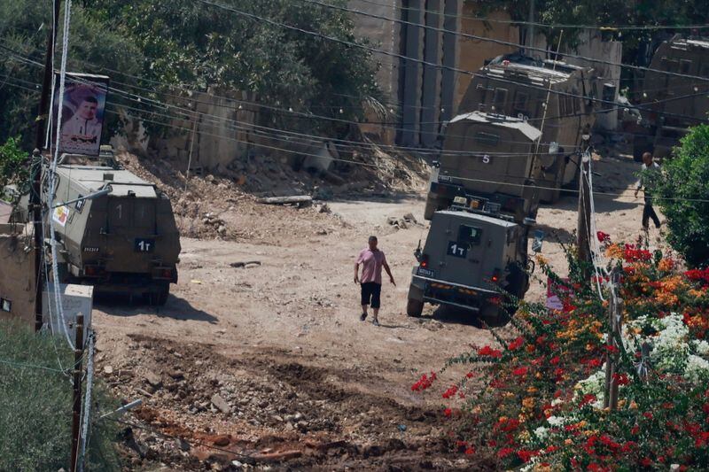 Un hombre palestino camina cerca de vehículos militares israelíes durante una redada israelí en Yenin (REUTERS/Ammar Awad)