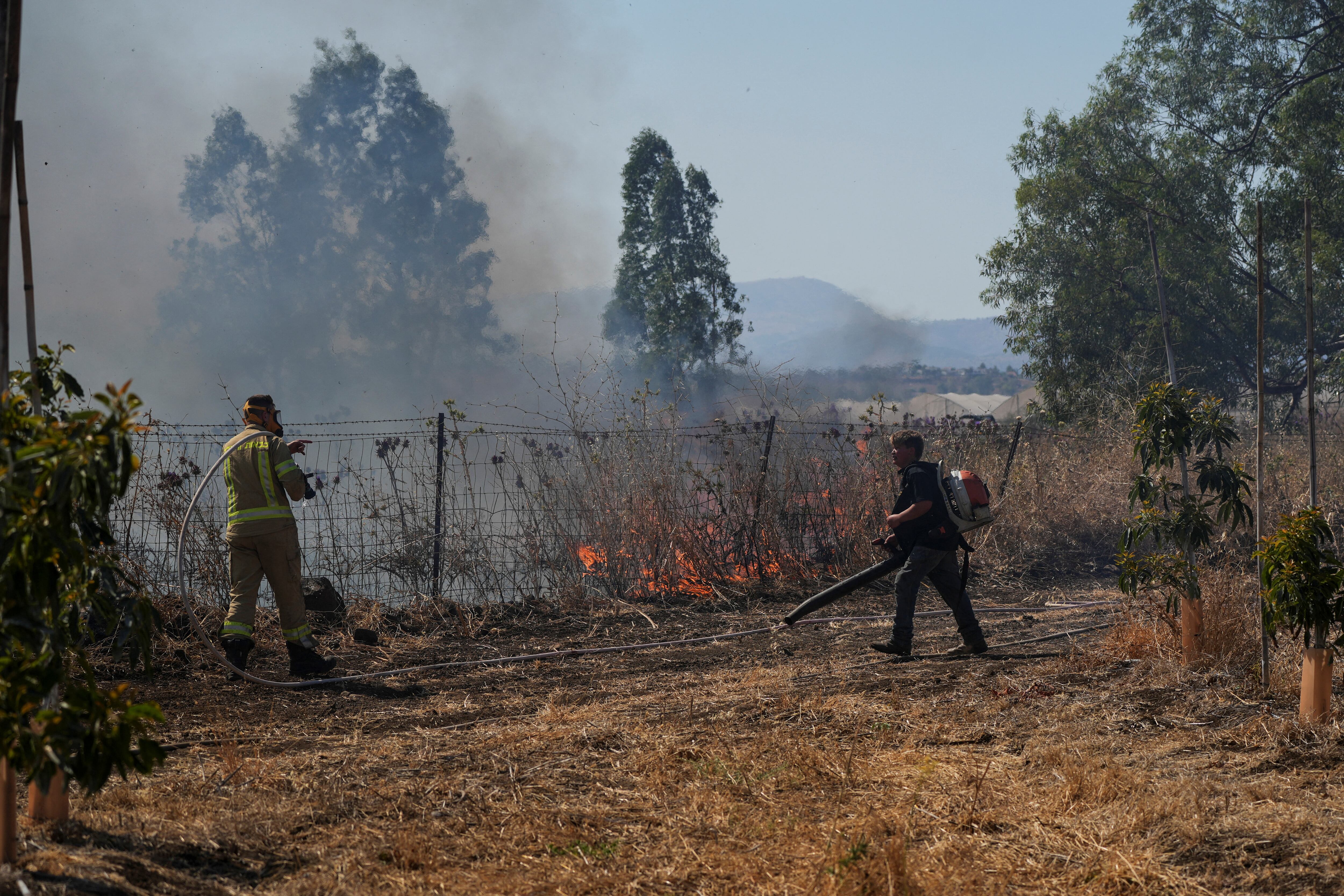 Un bombero israelí y otro hombre trabajan para controlar el fuego tras los ataques con cohetes desde el Líbano este martes (REUTERS/Ayal Margolin)