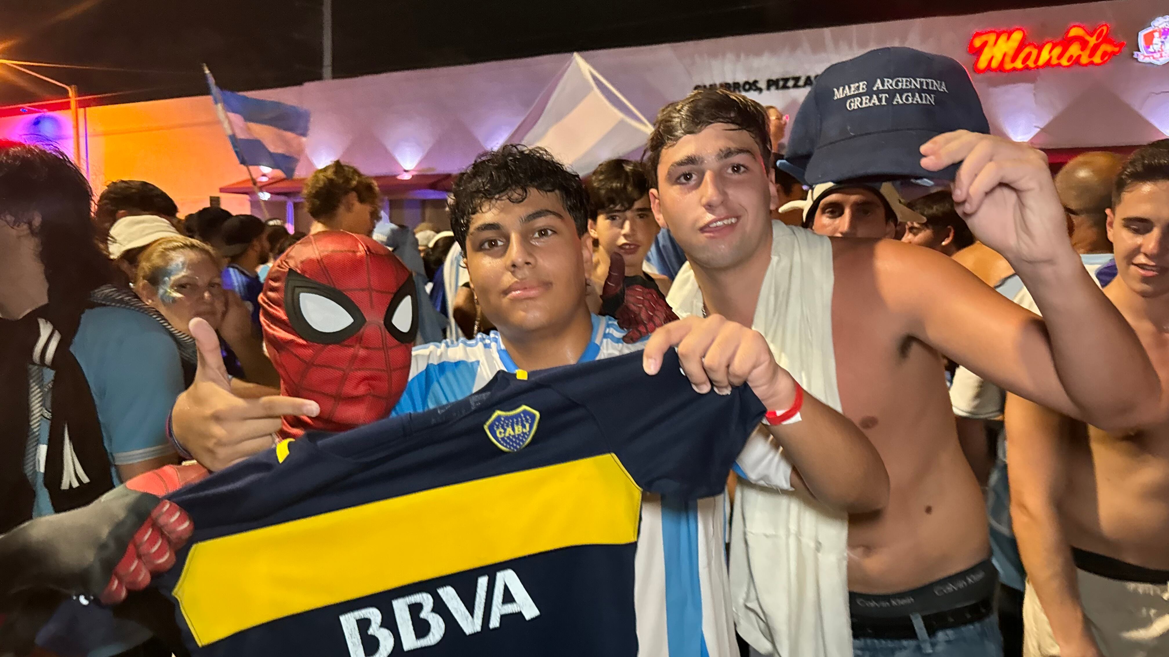 Una multitud de hinchas argentinos, vestidos con camisetas de la selección y agitando banderas celestes y blancas, celebra en las calles de Miami Beach durante la noche. La gente se muestra eufórica, tomando fotos y cantando, en una atmósfera festiva y llena de emoción tras la victoria de la Selección Argentina en la Copa América.